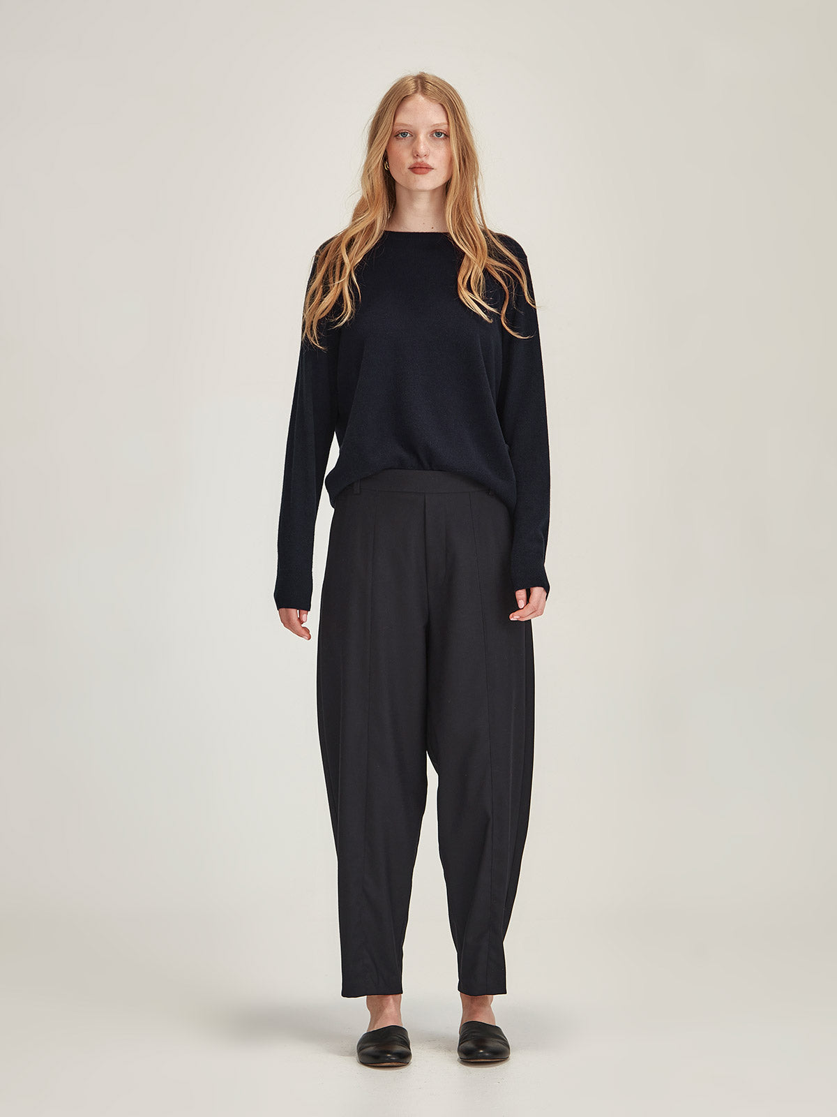 Woman wearing Caroline Sills Eleanor crew neck Cashmere Sweater in French Navy and Tobi Pant in Navy against grey backdrop