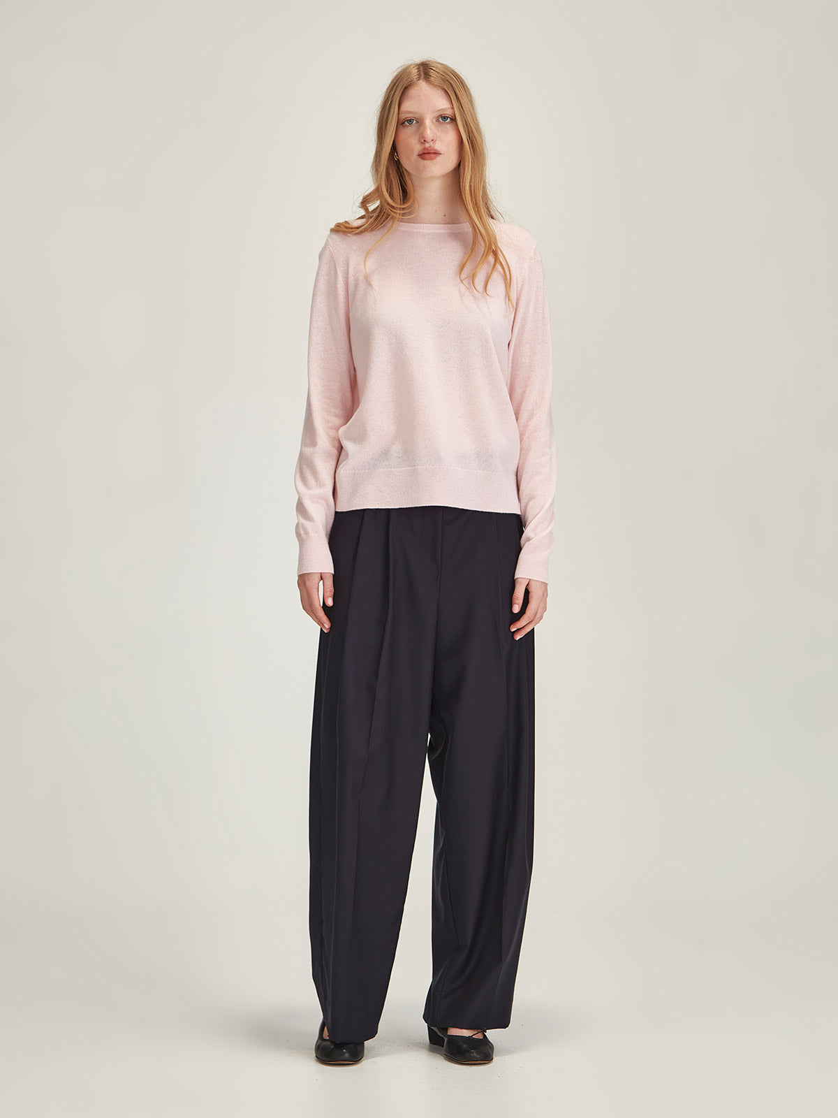 Woman wearing Caroline Sills Eleanor crew neck Cashmere Sweater in Pale Pink and Ashley Pant in Navy against grey backdrop