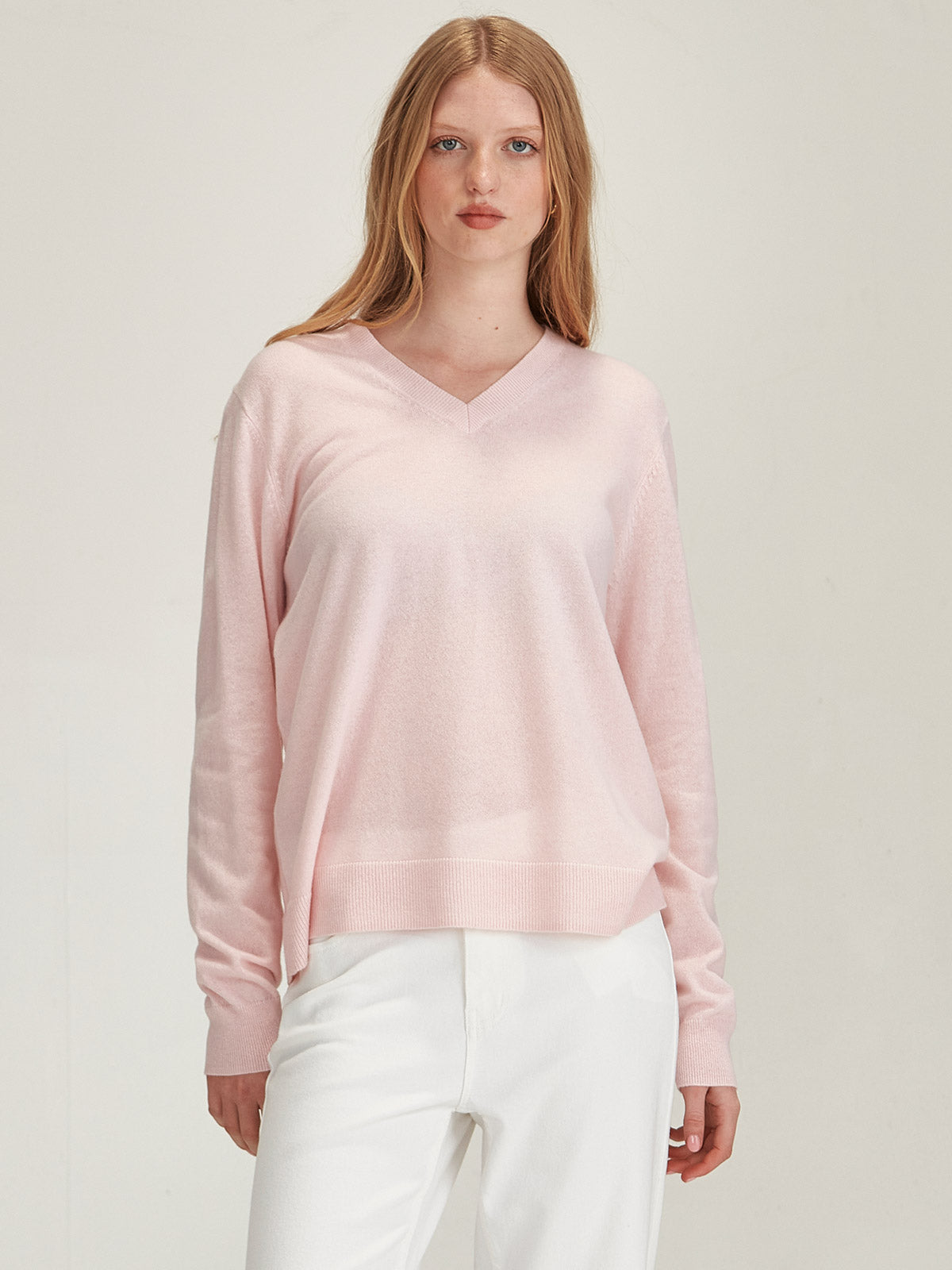 Close up of woman wearing Caroline Sills luxe Lucy Cashmere V Neck Sweater in Pale Pink colour against grey backdrop