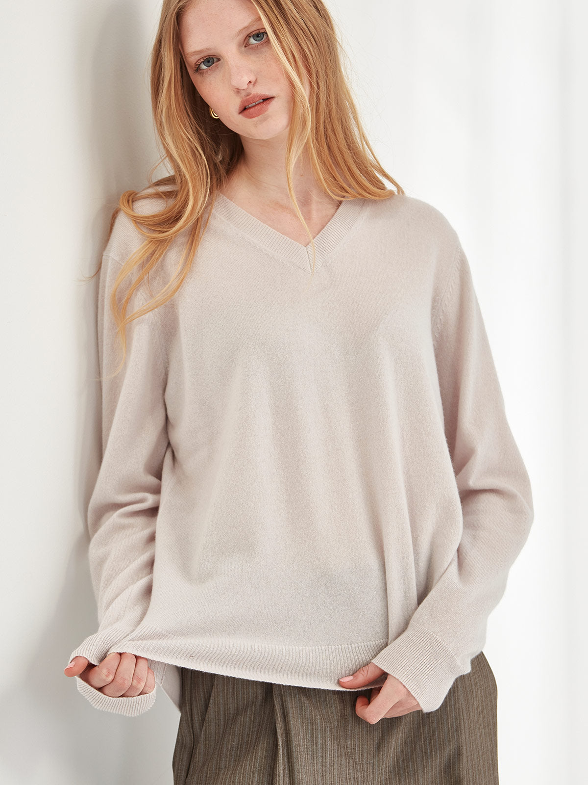 Close up of woman wearing Caroline Sills luxe Lucy Cashmere V Neck Sweater in Vapour beige colour against grey backdrop