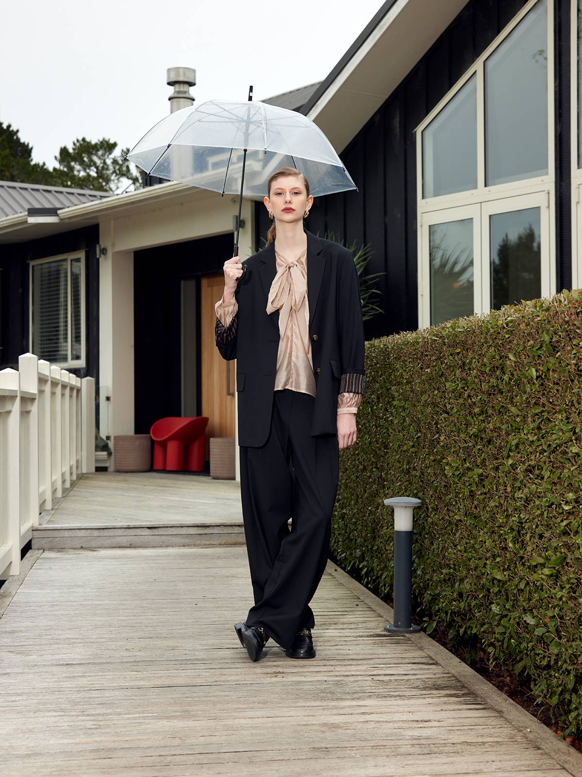 Woman wearing Caroline Sills merino wool suit - Ashley Pleat Pant and Maxine Blazer - outside home with clear umbrella.