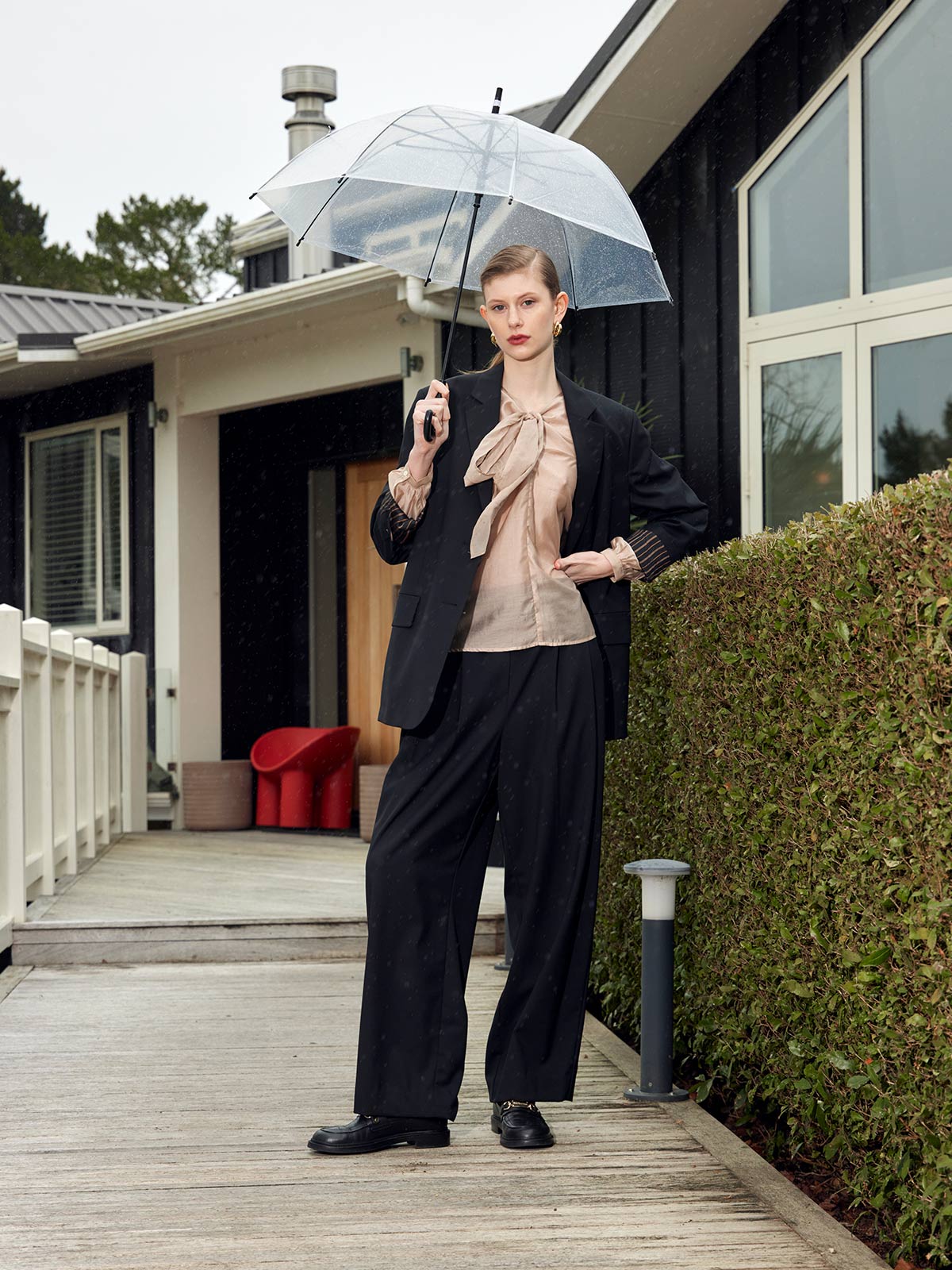 Woman wearing Caroline Sills merino wool suit - Ashley Pleat Pant and Maxine Blazer - outside home with clear umbrella.