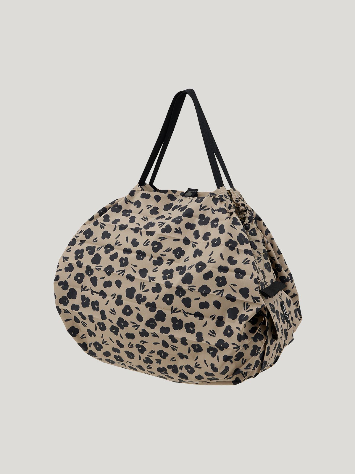 Foldable, reusable shopping bag with a black and beige print that abstractly mimics paw prints or leopard spots on a grey background.