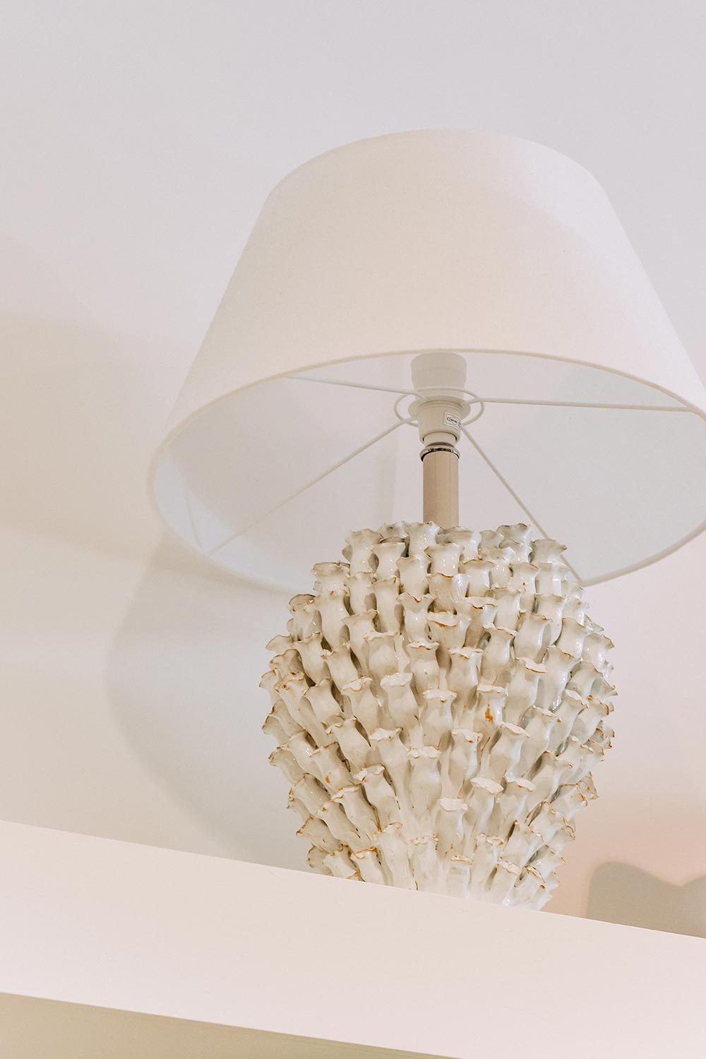 Designer ceramic lamp with a sculptural barnacle inspired base and white fabric shade, styled on a shelf at Sills + Co.