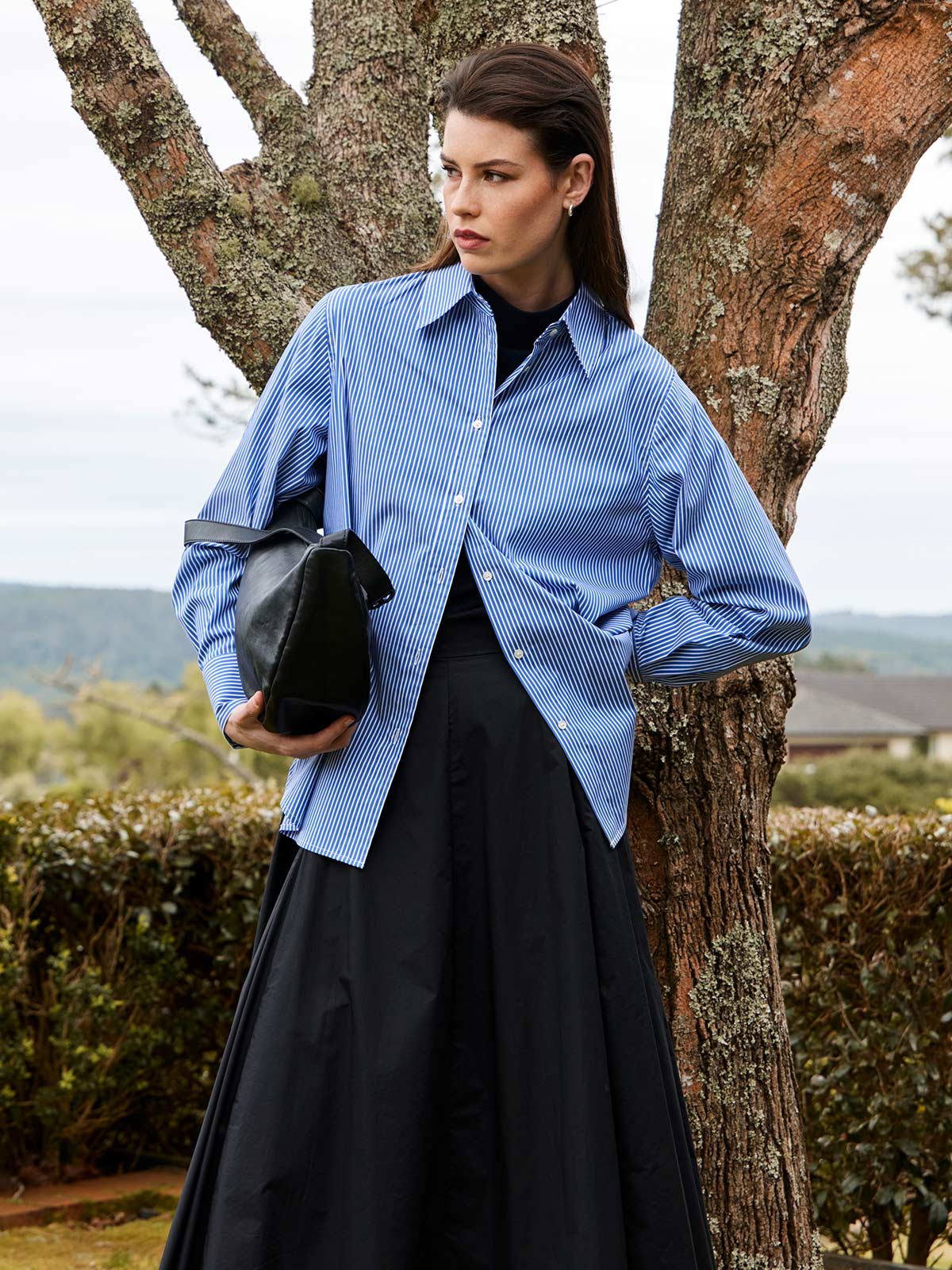 close up of women outdoors wearing Sills navy blue Princeton Striped Shirt, black Zaiya Godet Skirt, and Juju & Co Sling bag