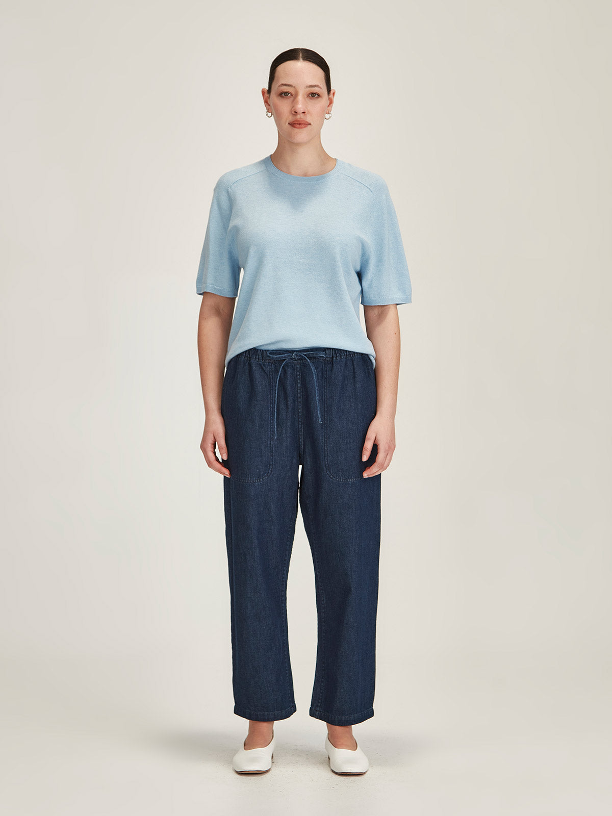 woman wearing a baby blue Sills Cecilia knitted Tee t-shirt and dark denim Ginza cropped jeans on grey background