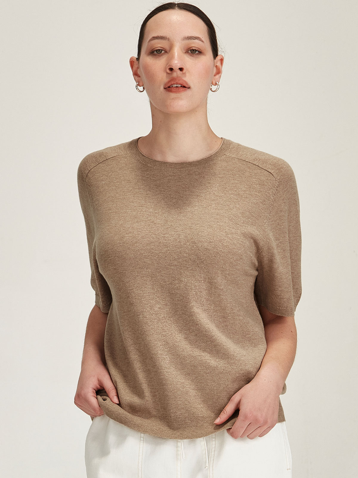 close up of a woman wearing a beige Sills Cecilia knitted Tee t-shirt on grey background