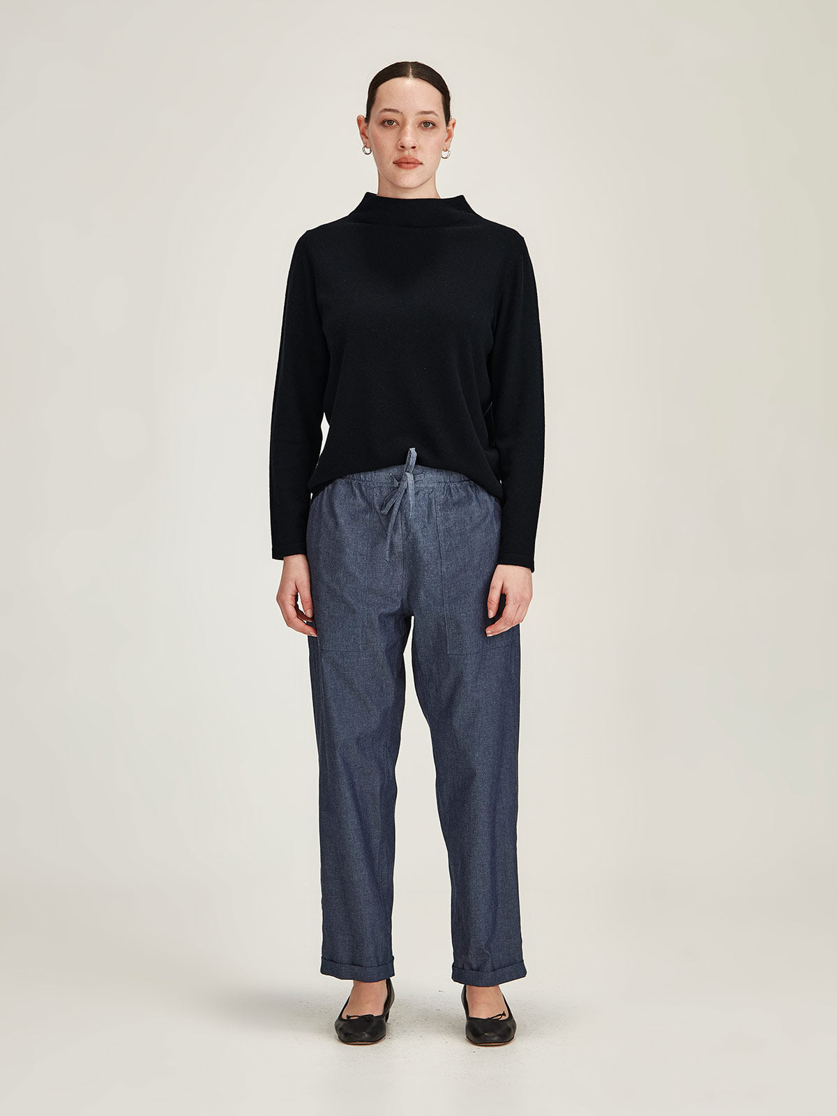 woman wearing navy Sills Tasmin funnel neck sweater with indigo Serena Chambray denim pant against grey background