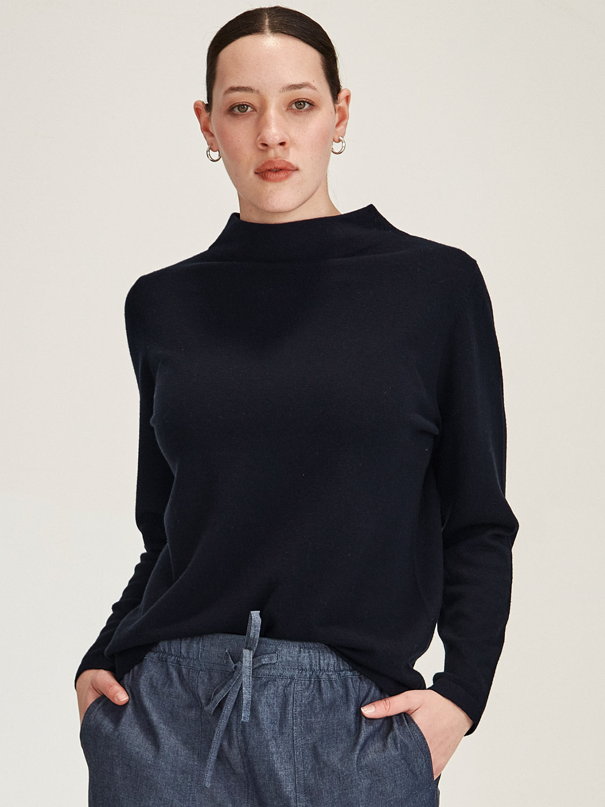 close up of woman wearing navy Sills Tasmin funnel neck sweater against grey background