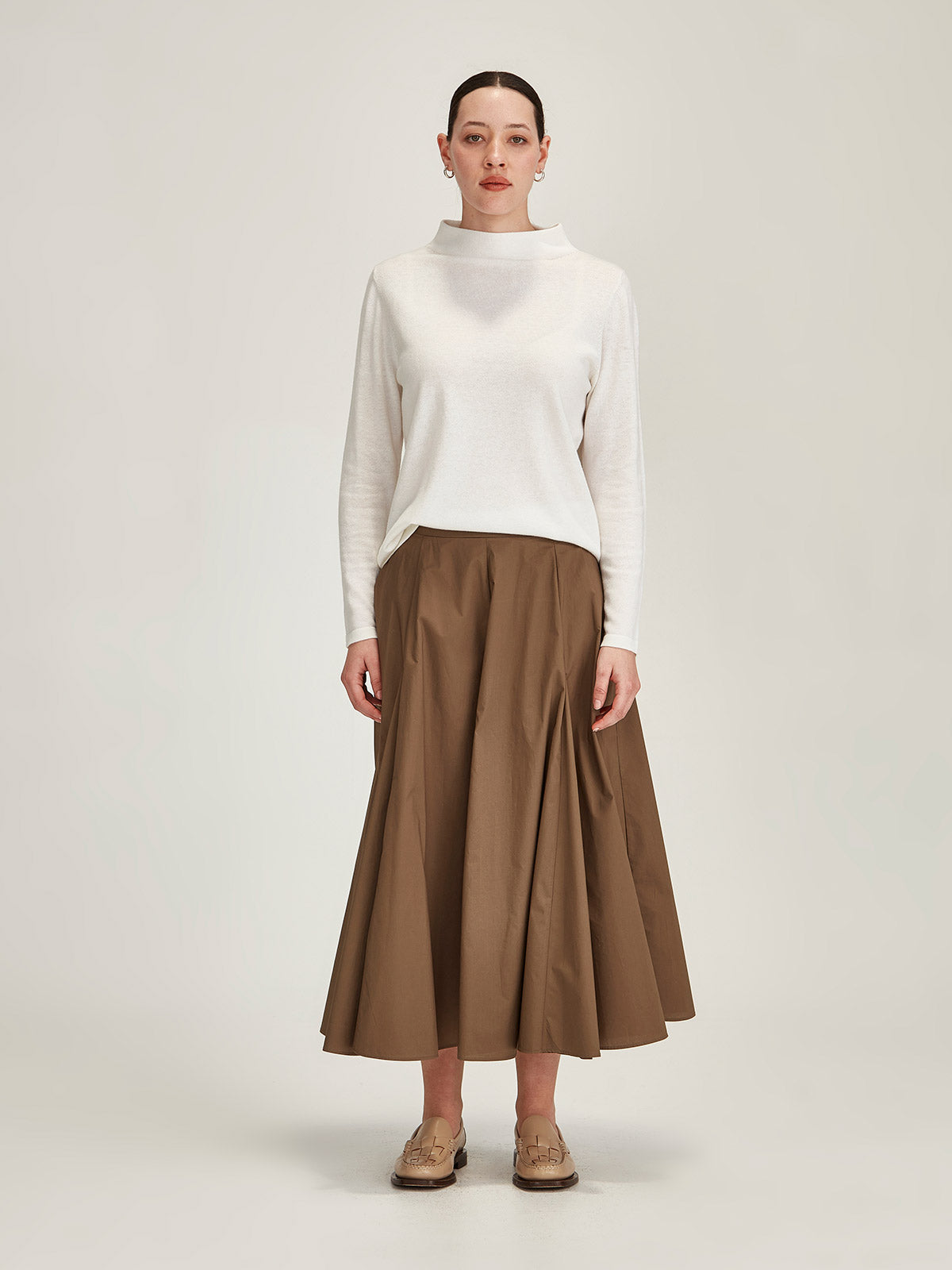 woman wearing off white Sills Tasmin funnel neck sweater with broze Zaiya godet midi skirt against grey background