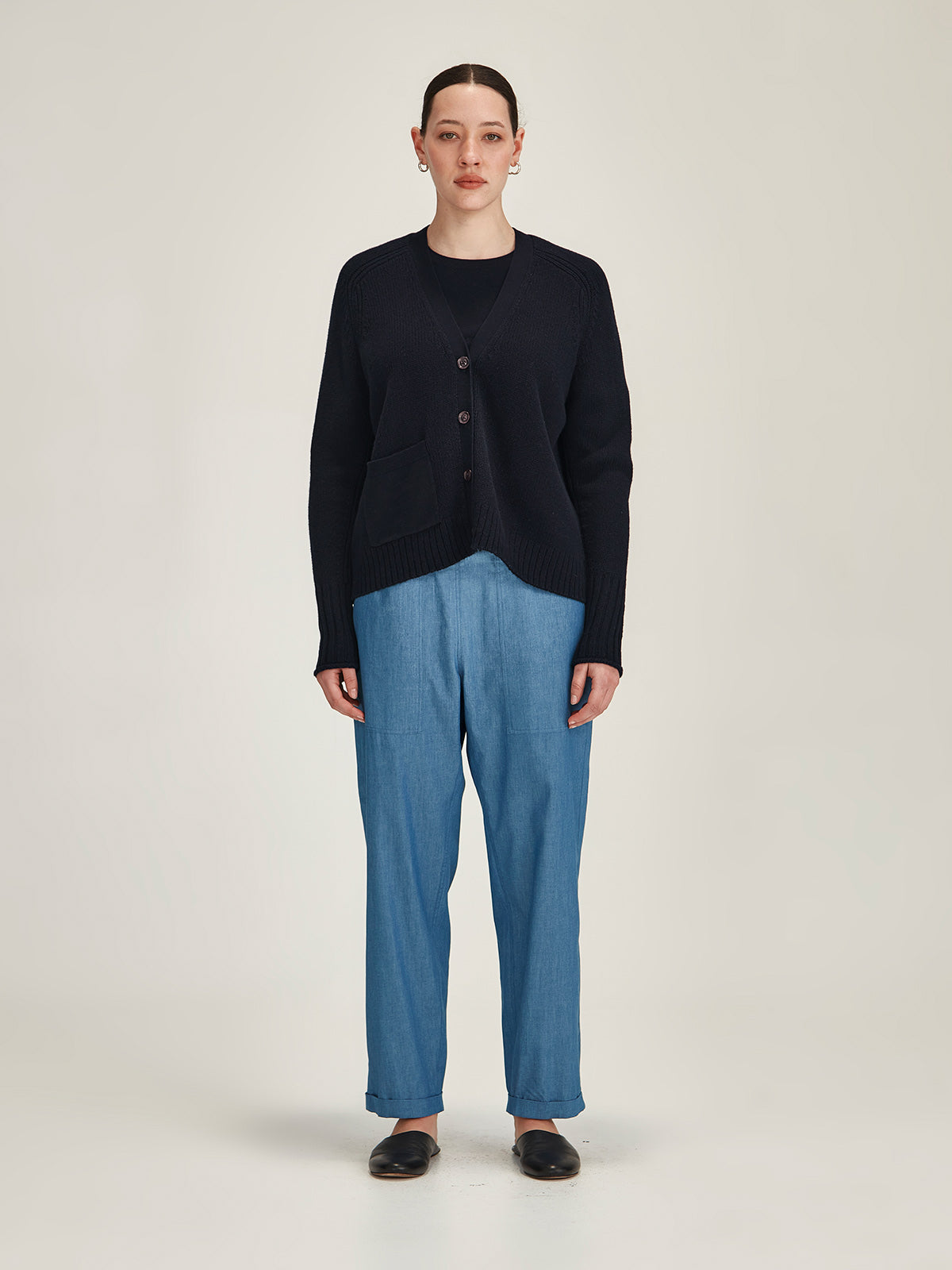 woman wearing Sills navy merino wool/cotton knitted Yuri Cardigan with denim Serena Chambray pant in front of grey background