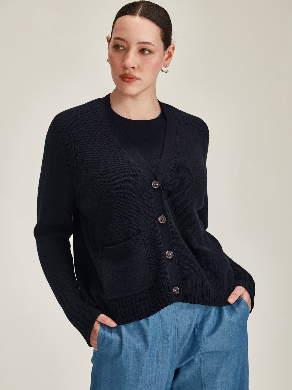 close up of woman wearing Sills navy knitted merino/cotton Yuri Cardigan against grey background