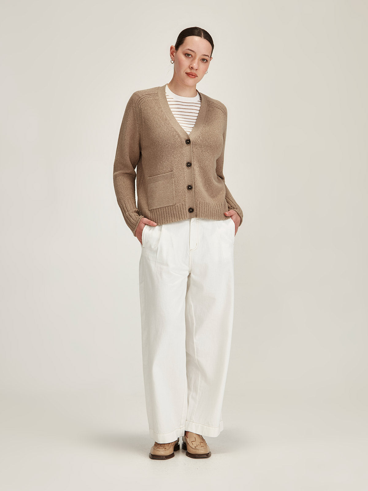 woman wearing Sills beige merino wool/cotton knitted Yuri Cardigan with white denim Britt jeans in front of grey background
