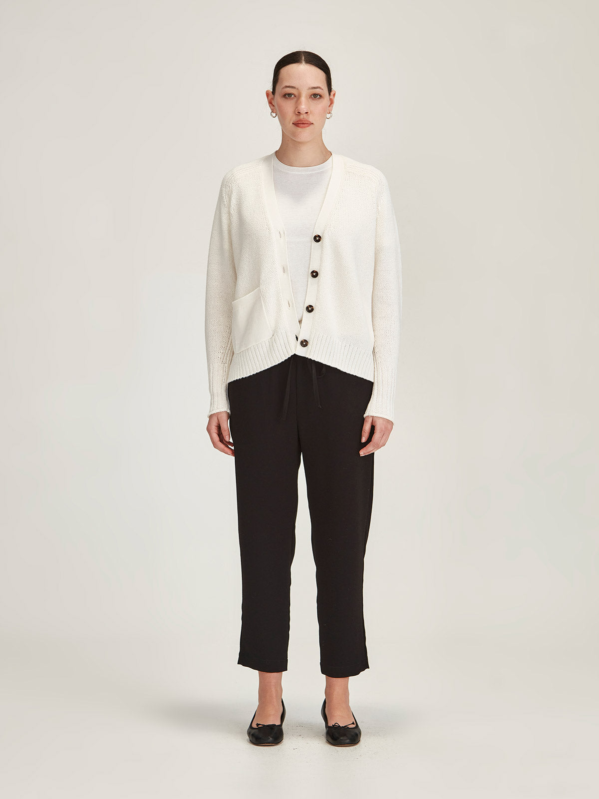 woman wearing Sills off white merino wool/cotton knitted Yuri Cardigan with black cropped Romily pant in front of grey background