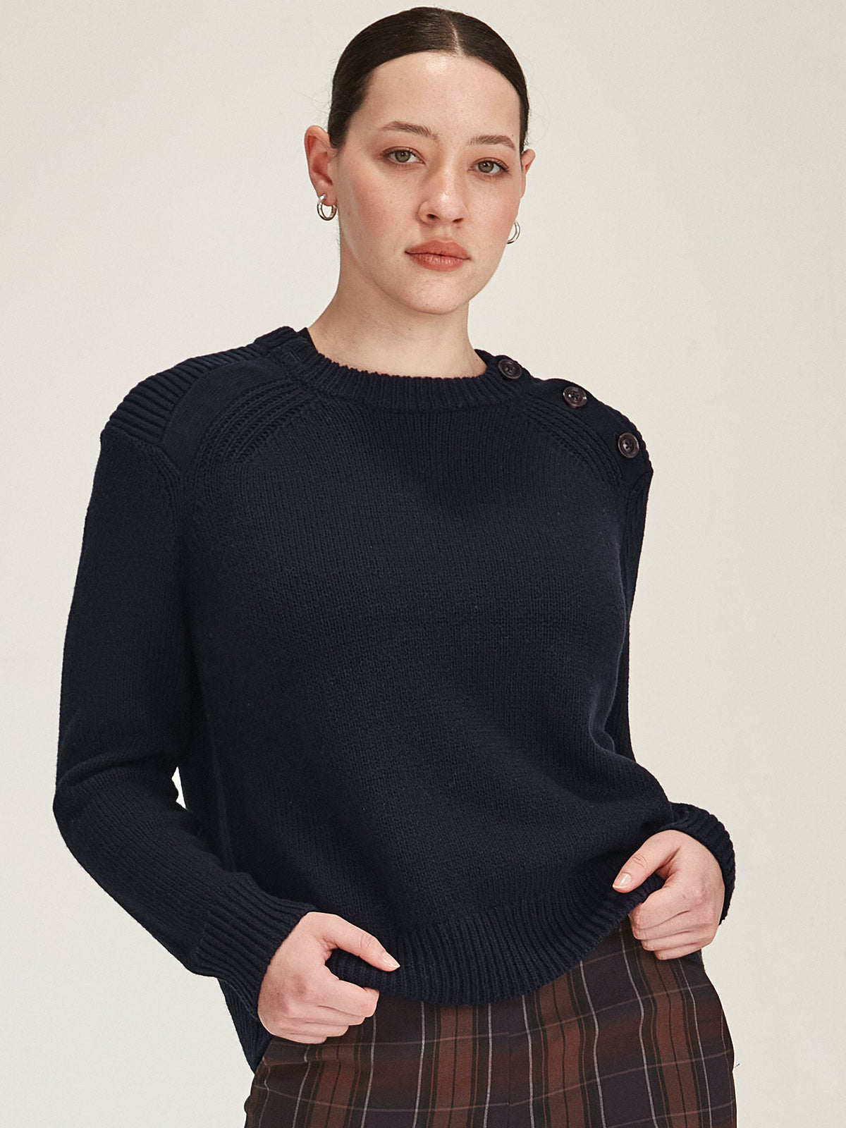 close up of woman wearing navy Sills merino/cotton knitted Colette jumper with buttons on shoulder against grey background