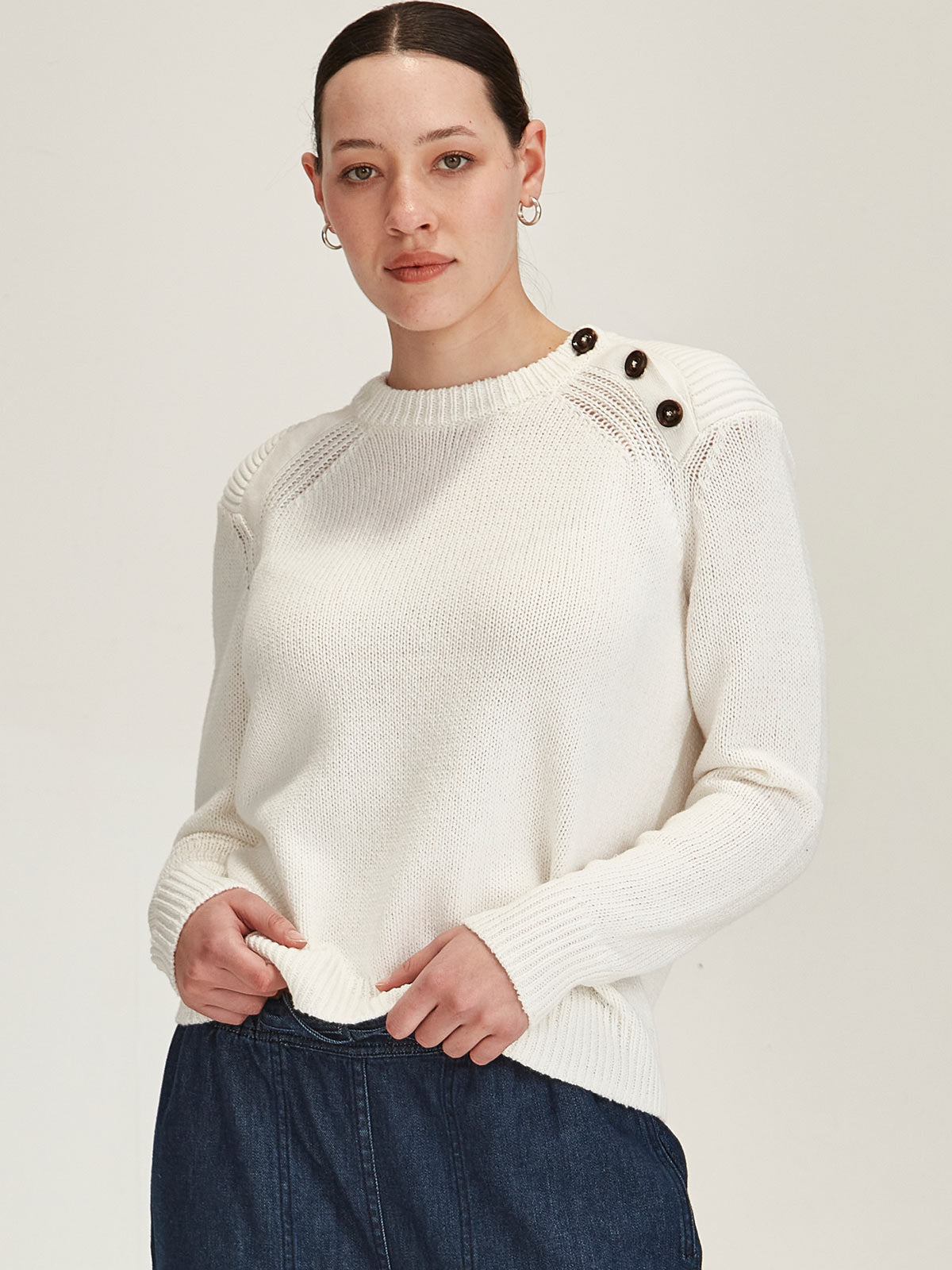 close up of woman wearing off white merino/cotton knitted Colette jumper with buttons on shoulder against grey background