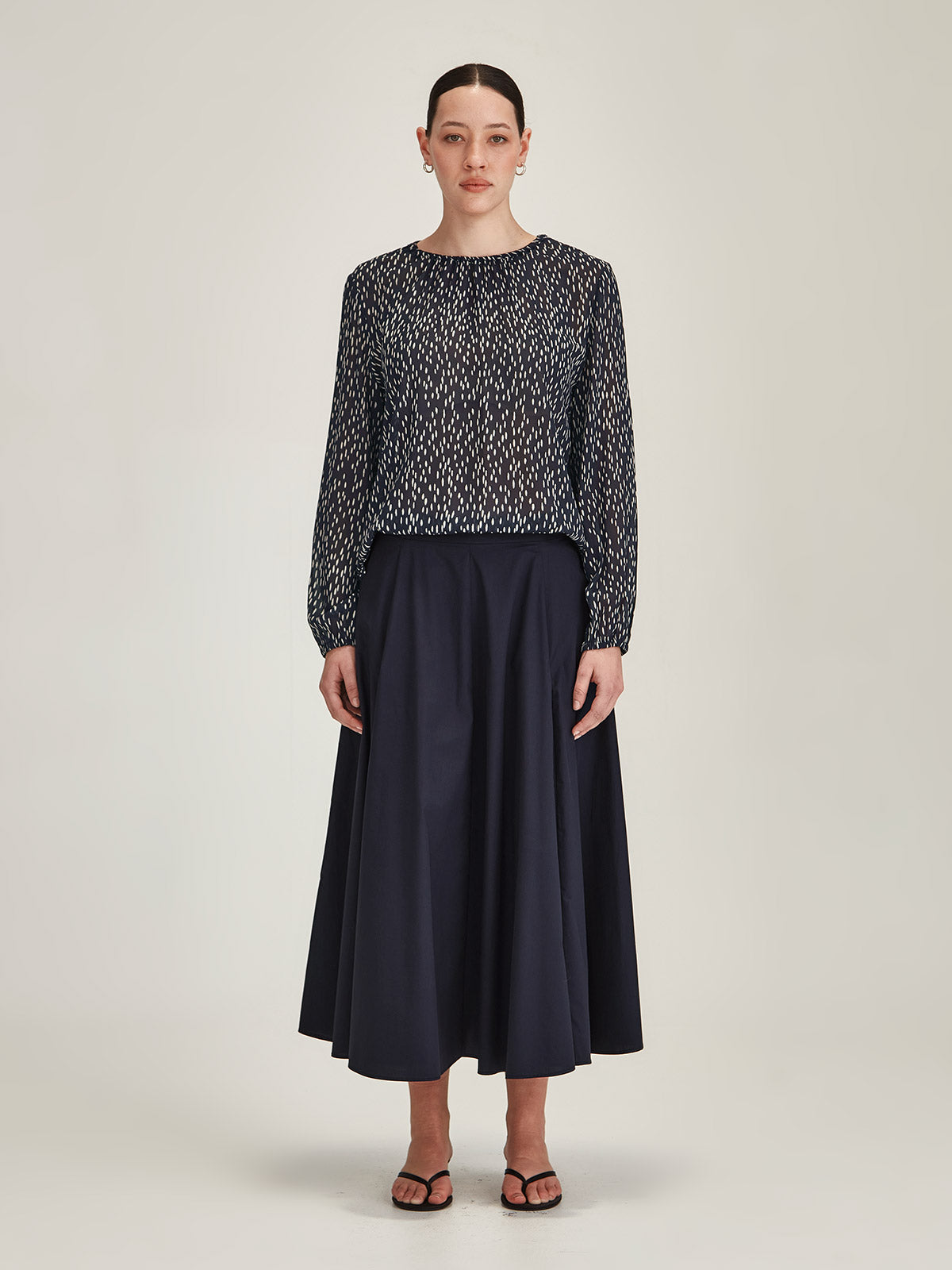 woman wearing Sills navy Anna Spot crepe blouse Top with navy Zaiya godet midi skirt against grey background