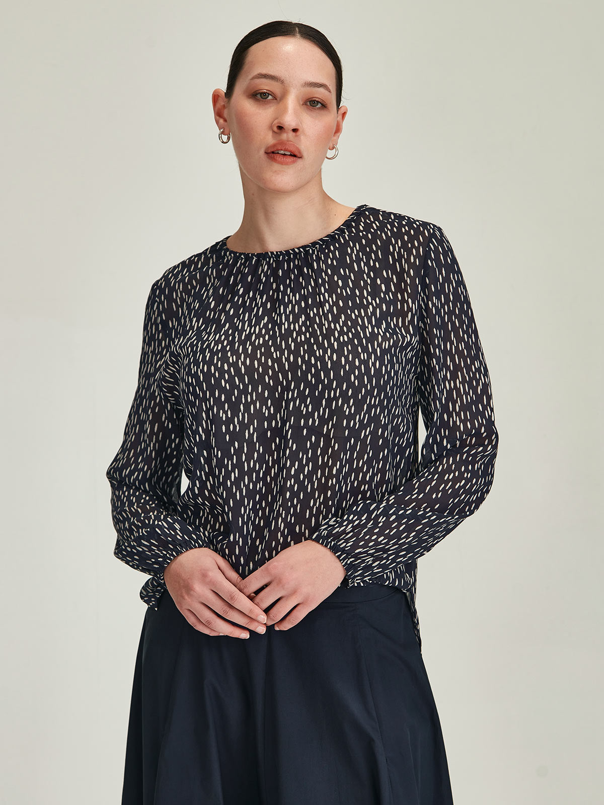 close up of woman wearing Sills Anna Spot polka dot crepe blouse Top in Navy blue against grey background