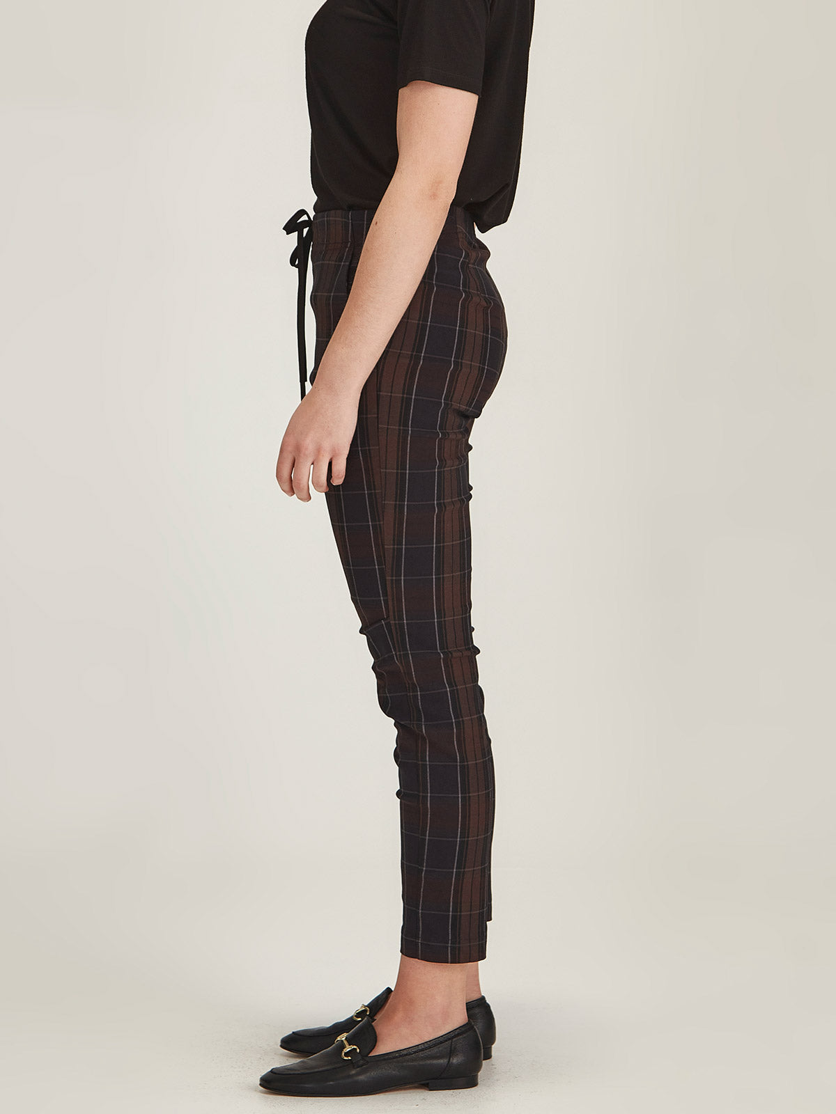 Close up of woman wearing Sills chocolate brown plaid print Emily Joggers on grey background