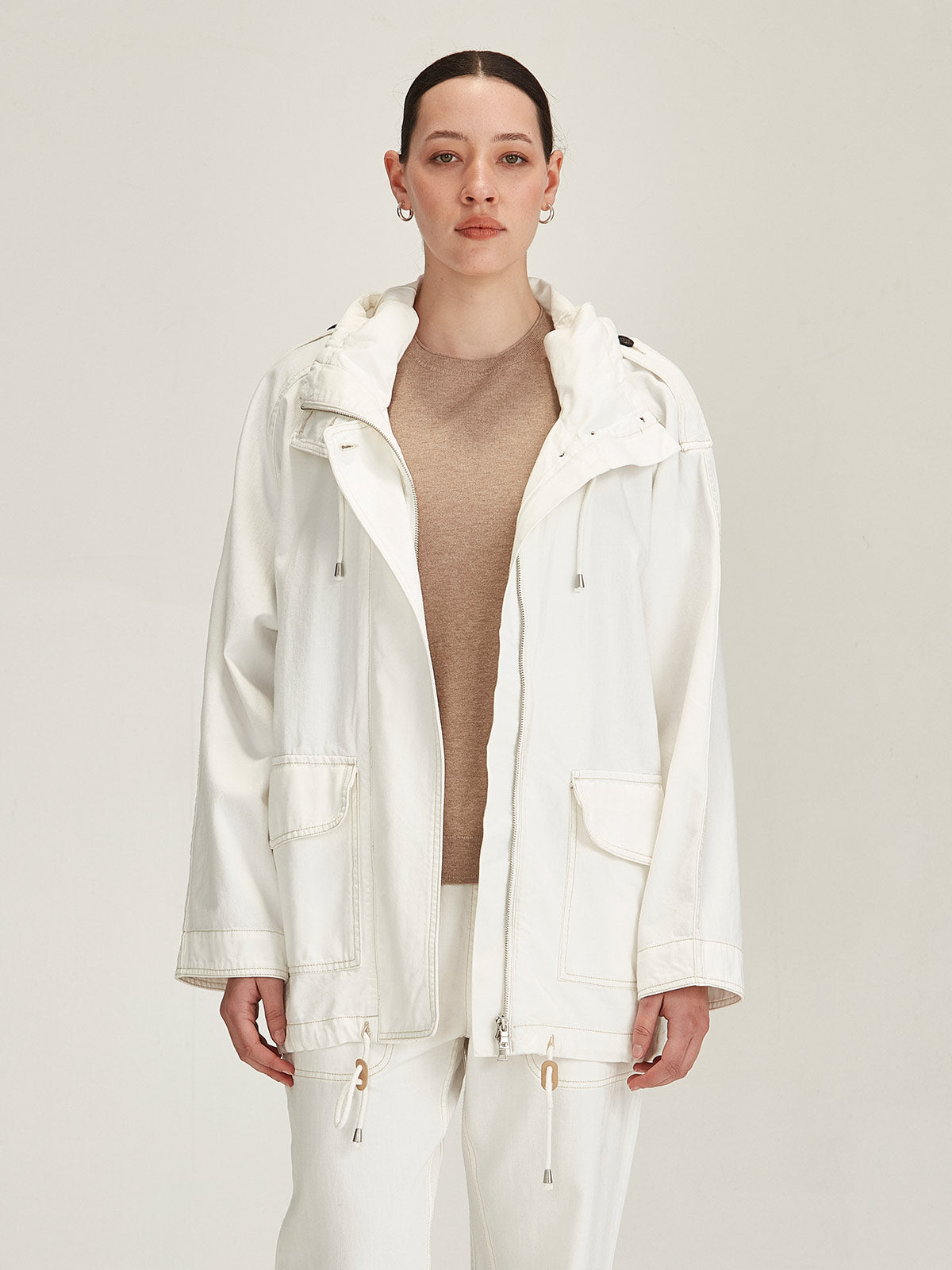 close up of woman wearing Sills white denim Dover Chalk Parka over a beige knitted t-shirt against grey background