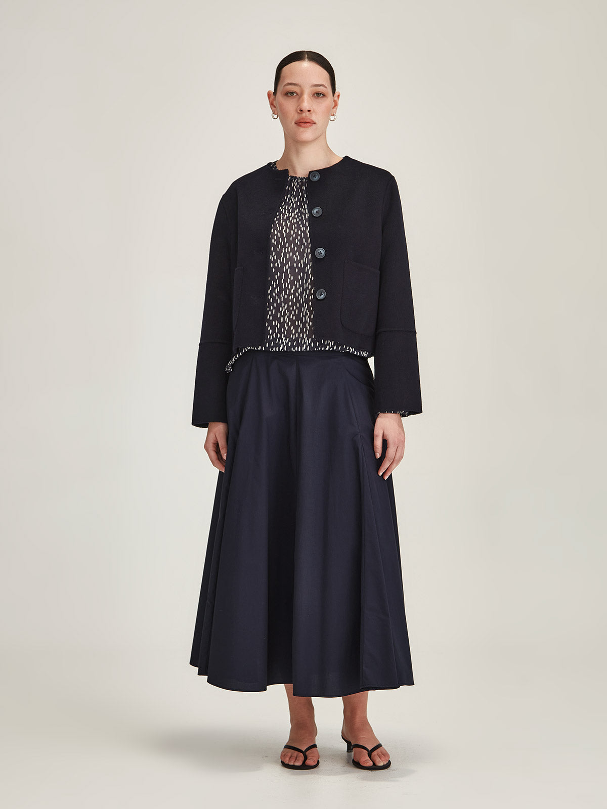 Woman wearing Sills navy Emiko wool and cashmere blend jacket with navy Zaiya godet midi skirt on grey background