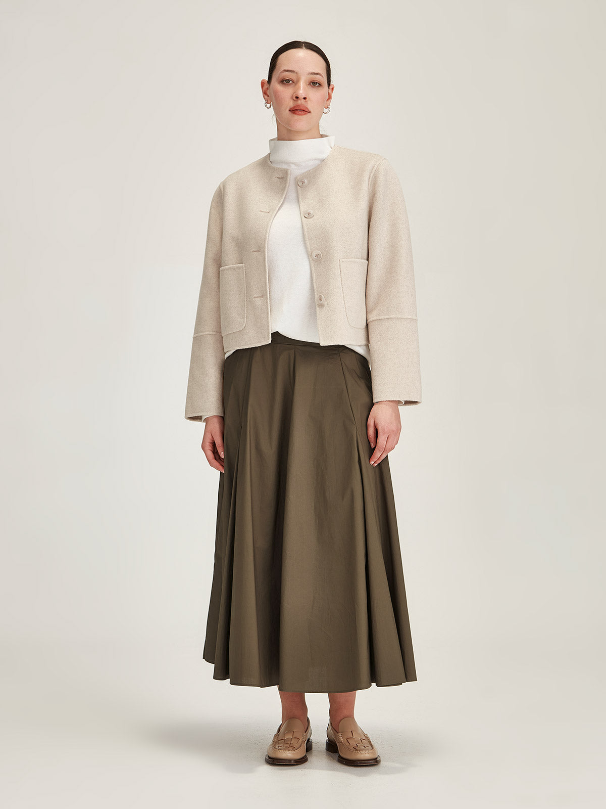 Woman wearing Sills cream Emiko wool and cashmere blend jacket with khaki Zaiya godet midi skirt on grey background