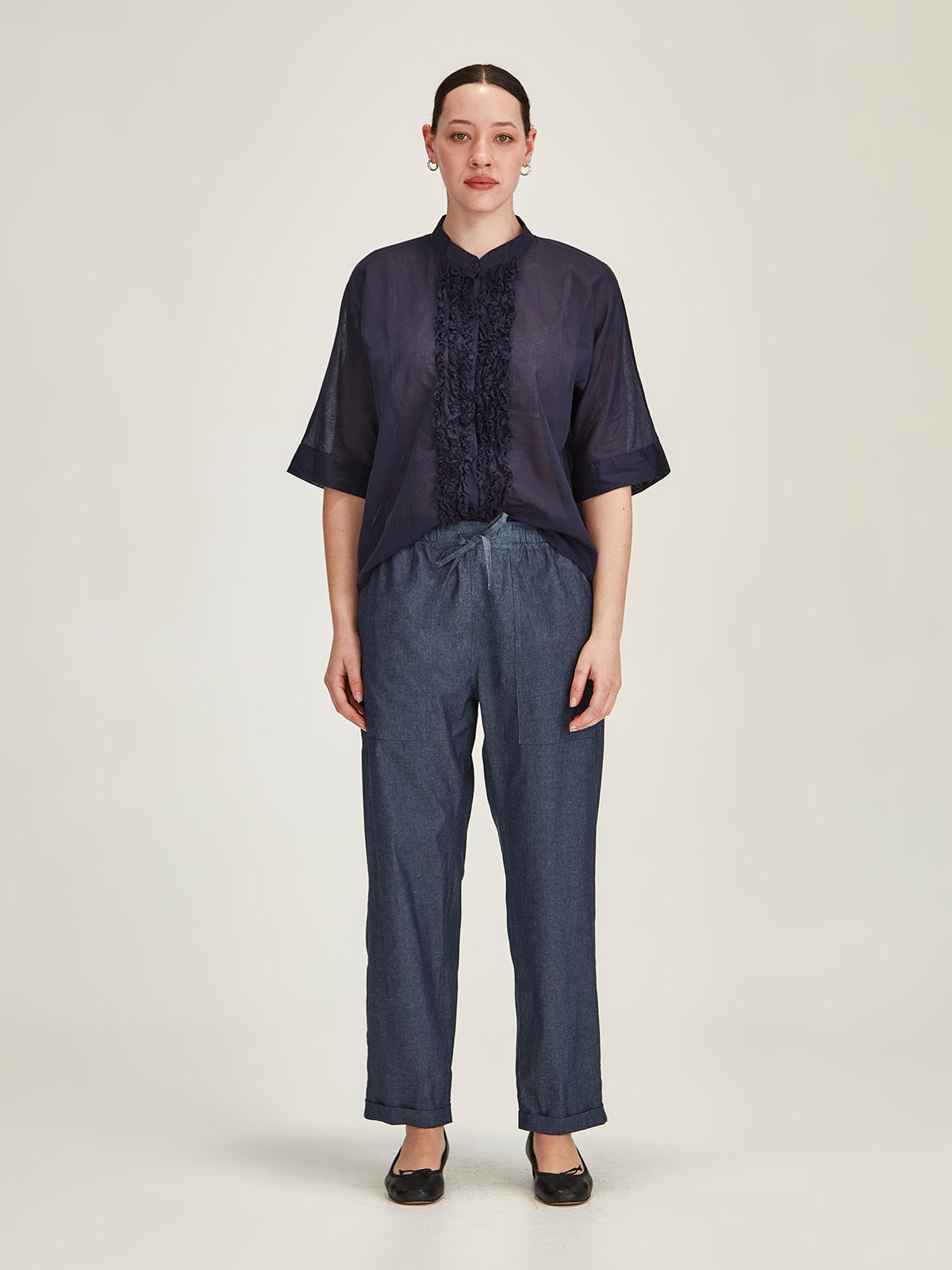 Woman in front of grey background wearing Sills Serena dark indigo Chambray jogger Pant and french navy Sasha Ruffle Blouse