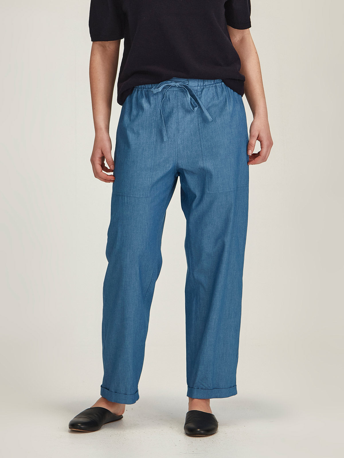 Close up of woman wearing Sills light indigo Serena Chambray Pant with drawstring waist in front of a grey background