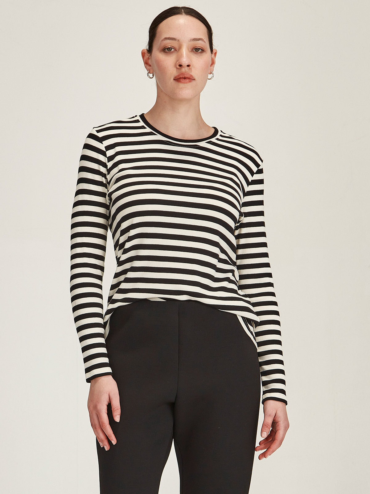 close up of woman in front grey background wearing black and ivory striped crew neck long sleeve t-shirt