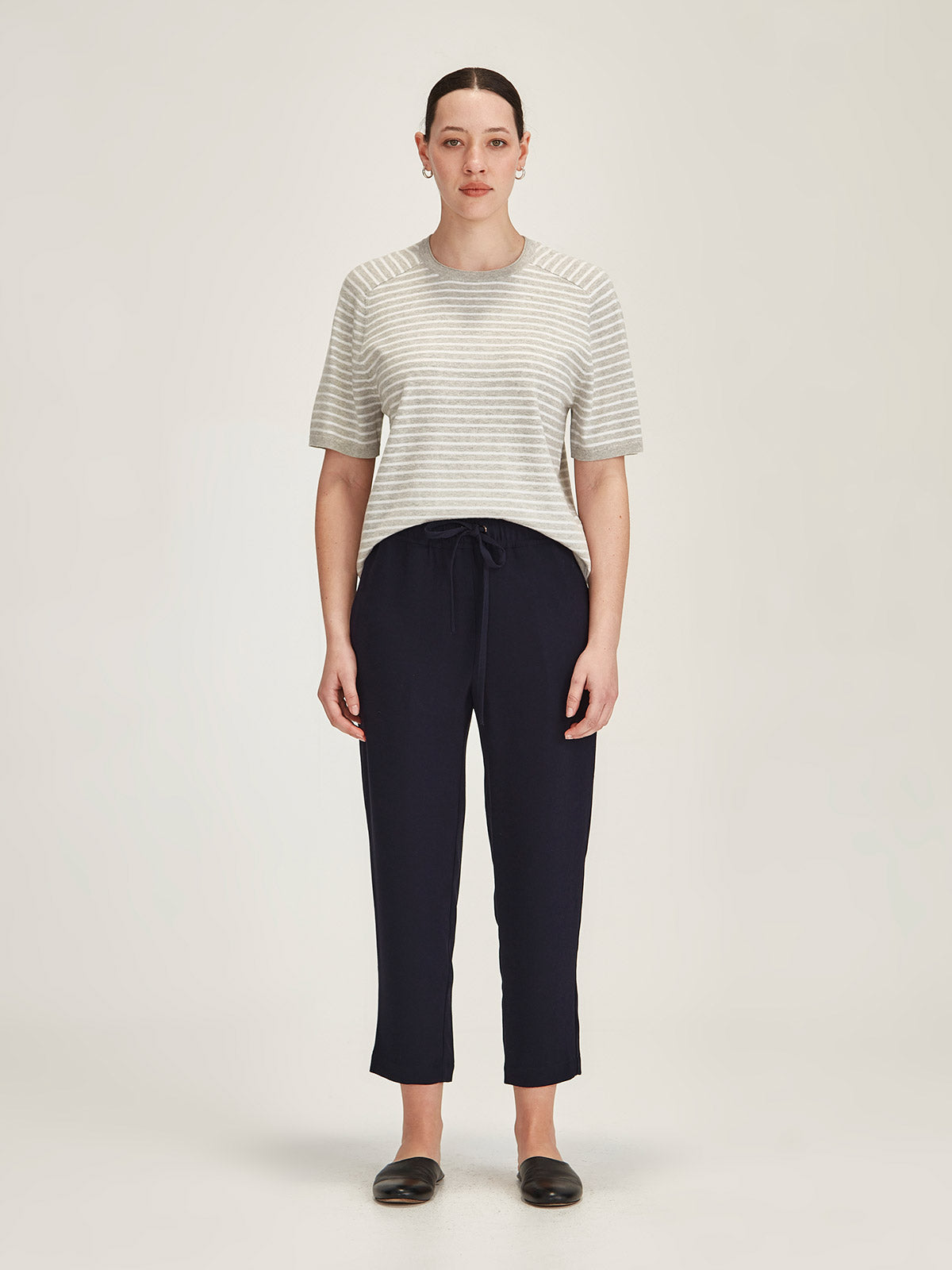 Woman wearing Sills navy Joseph crepe Romily Pant with Cecila Stripe Knitted T-shirt on grey background