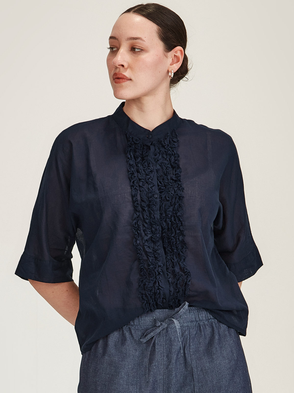 Close up of model wearing Sills Sasha Ruffle blouse in navy organic cotton in front of grey background