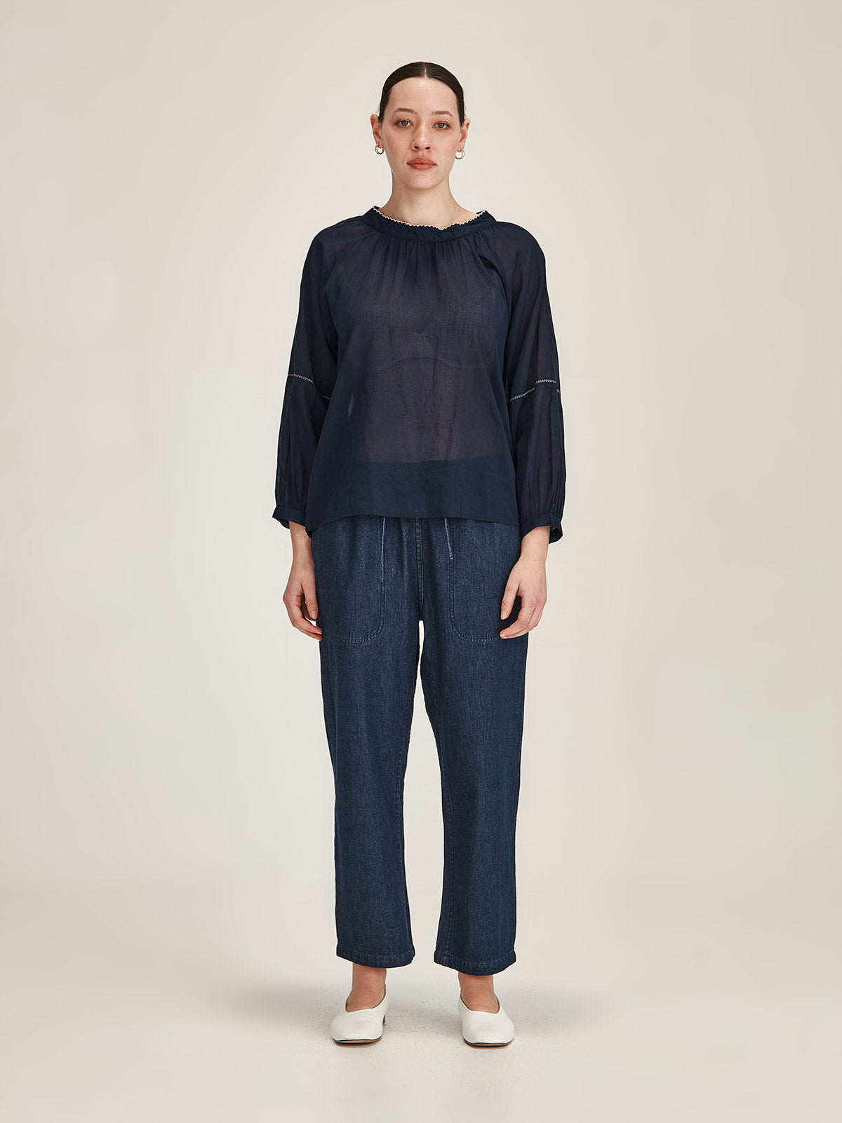Model wears a Sills navy organic cotton Hana Embroidered Top with dark denim Ginza Drawstring Jeans on grey background