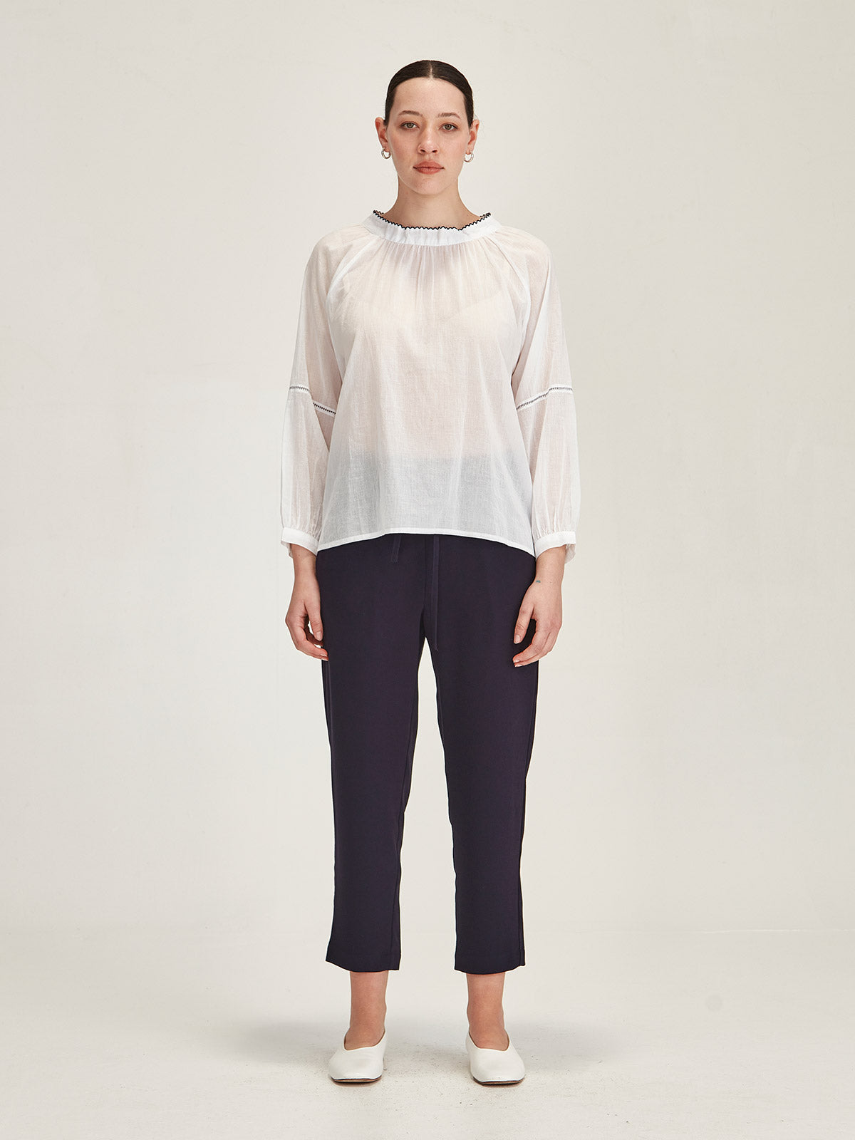 Model wearing a Sills white organic cotton Hana Embroidered Top with navy Romily cropped pants in front of grey background