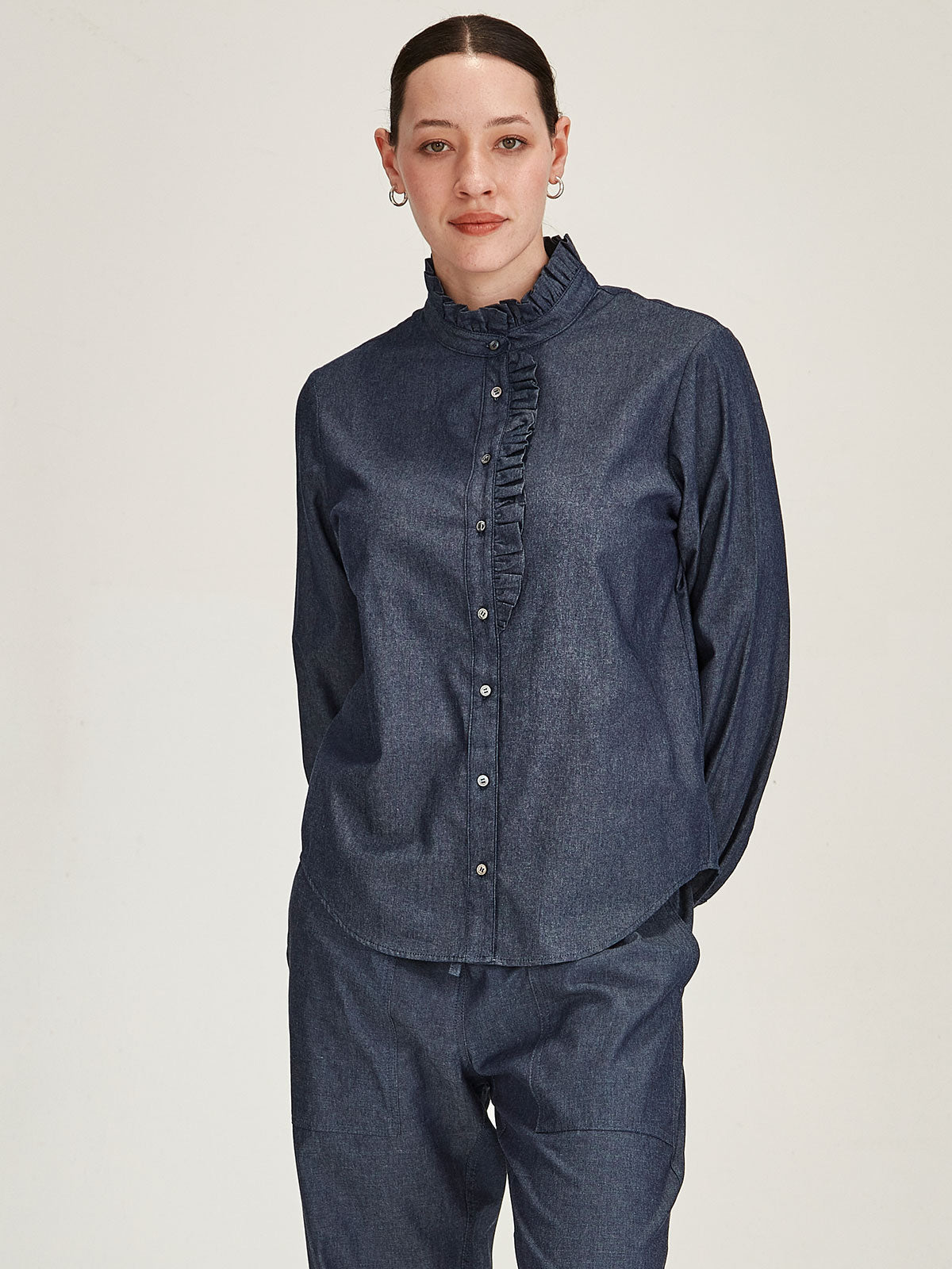 Close up of woman wearing Sills Mira Ruffle Blouse in dark indigo chambray with ruffle collar and lapel on grey background