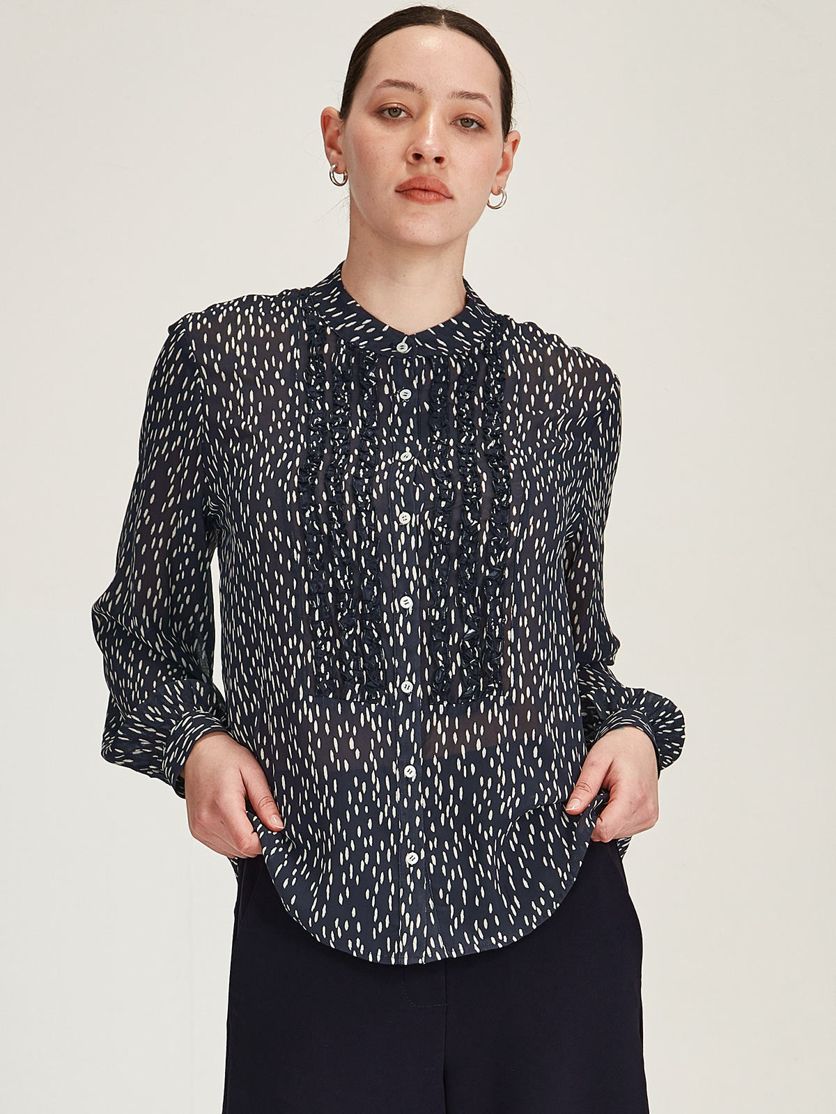 Close up of woman wearing navy Sills Ami Spot polka dot Shirt with ruffle detail front in front of grey background