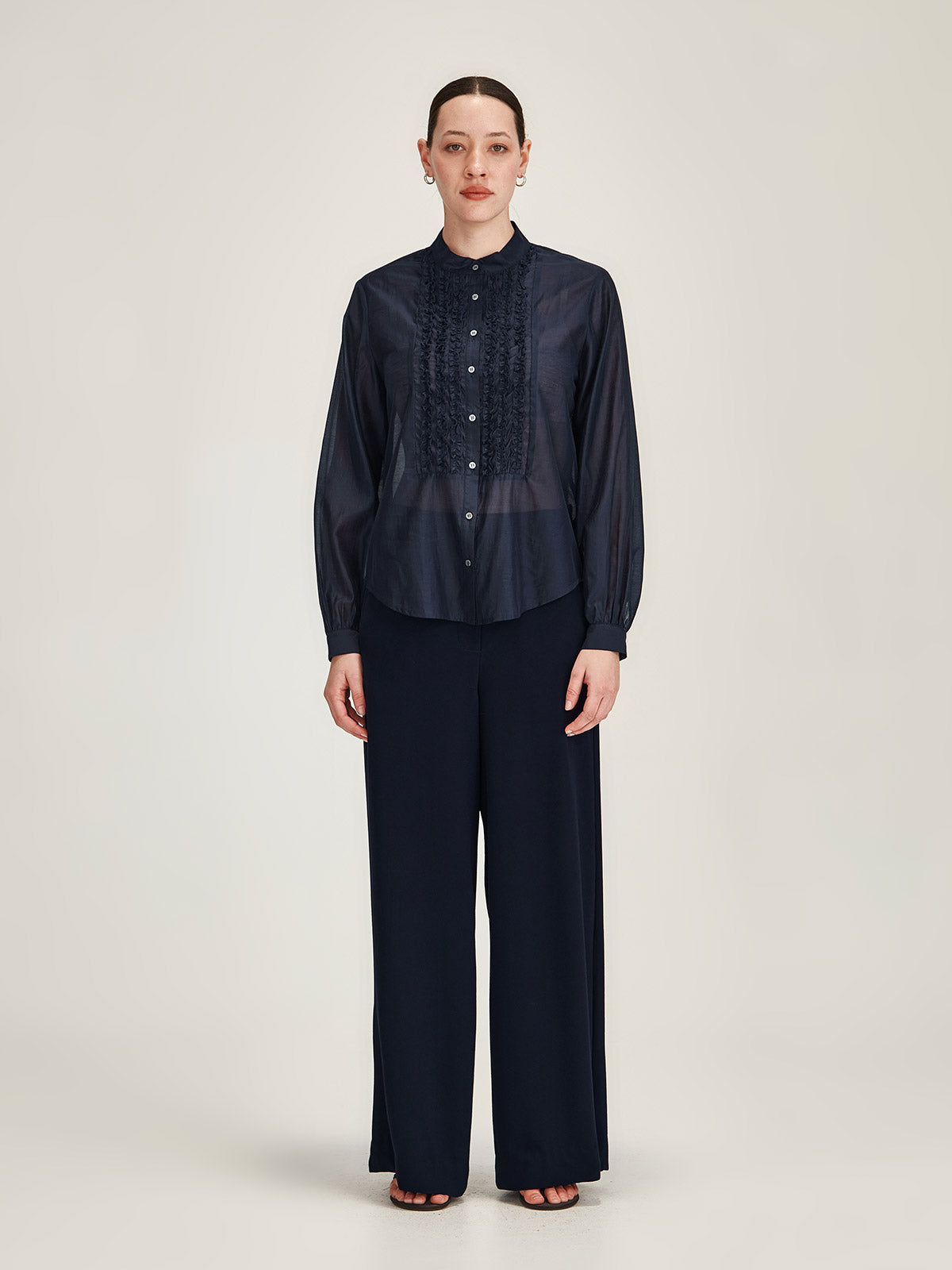 Woman wearing navy blue Sills Ami Shirt with ruffle detail front with navy Luca Wide Leg crepe pant against grey background