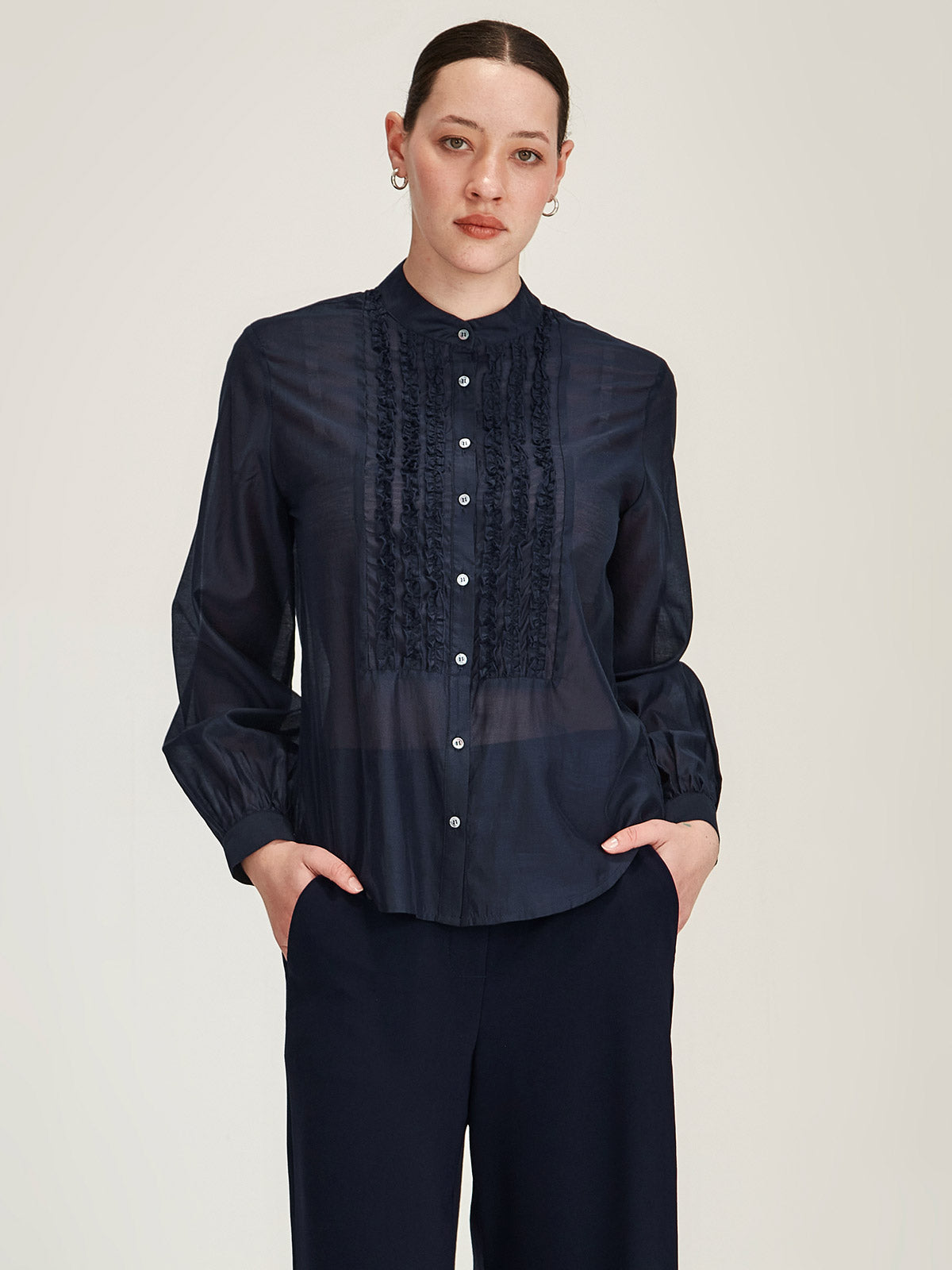 Close up of woman wearing navy blue Sills Ami Shirt with ruffle detail front in front of grey background
