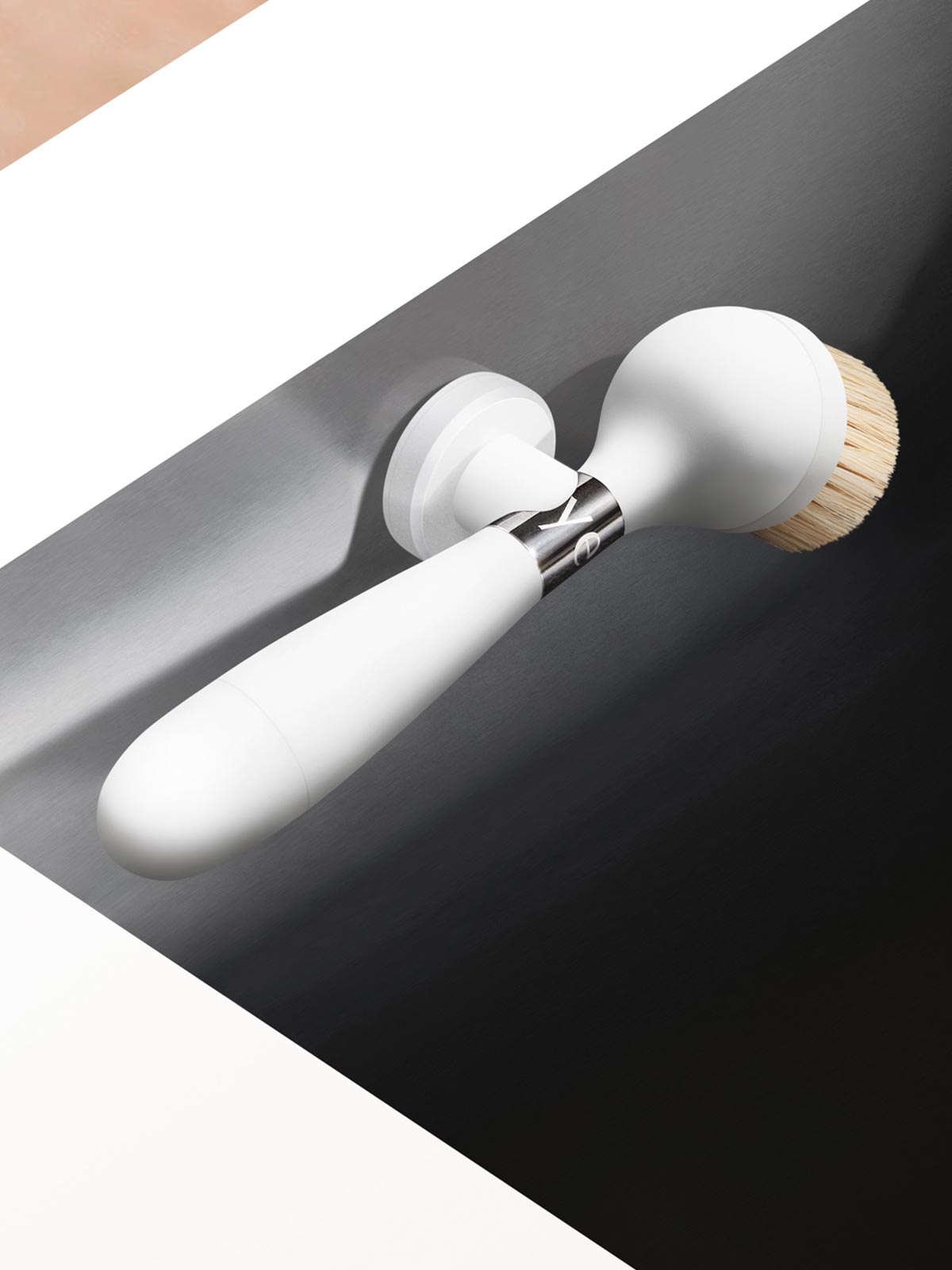 The One Brush V2 Suction by Yeseco - White version mounted on the edge of a dark undermount sink, showing the suction stand and natural sisal fibre brush head.