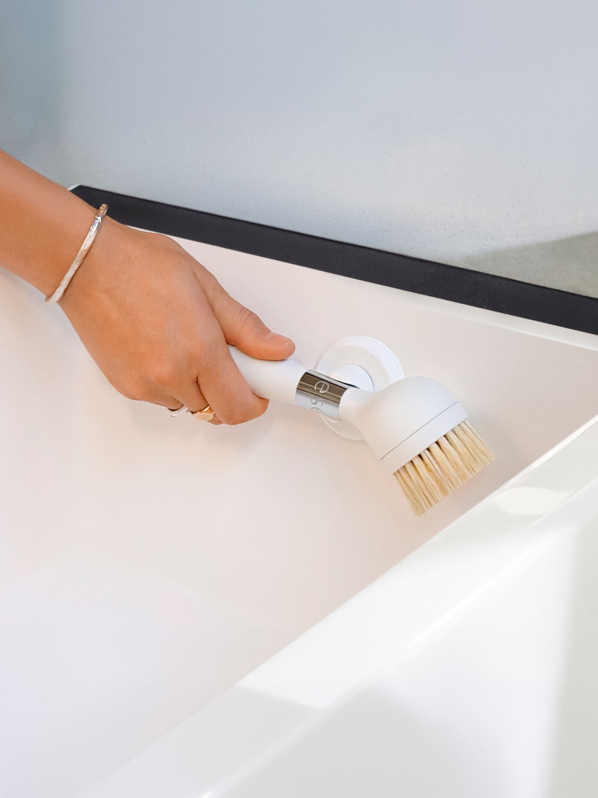 The One Brush V2 Suction by Yeseco - Hand scrubbing the inside of a white sink with the white brush, demonstrating the sisal fibre brush head in use.