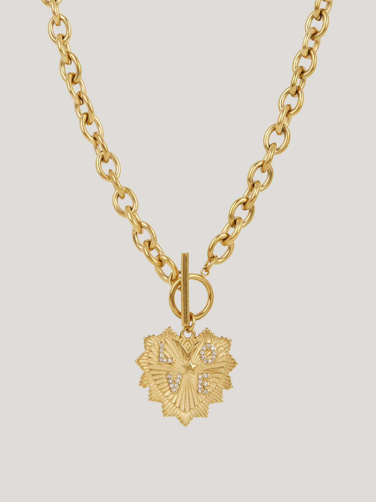A gold chain necklace featuring a textured,heart-shaped pendant adorned with small Cubic Zirconia letters spelling LOVE and a toggle clasp, shown against a solid light gray background.