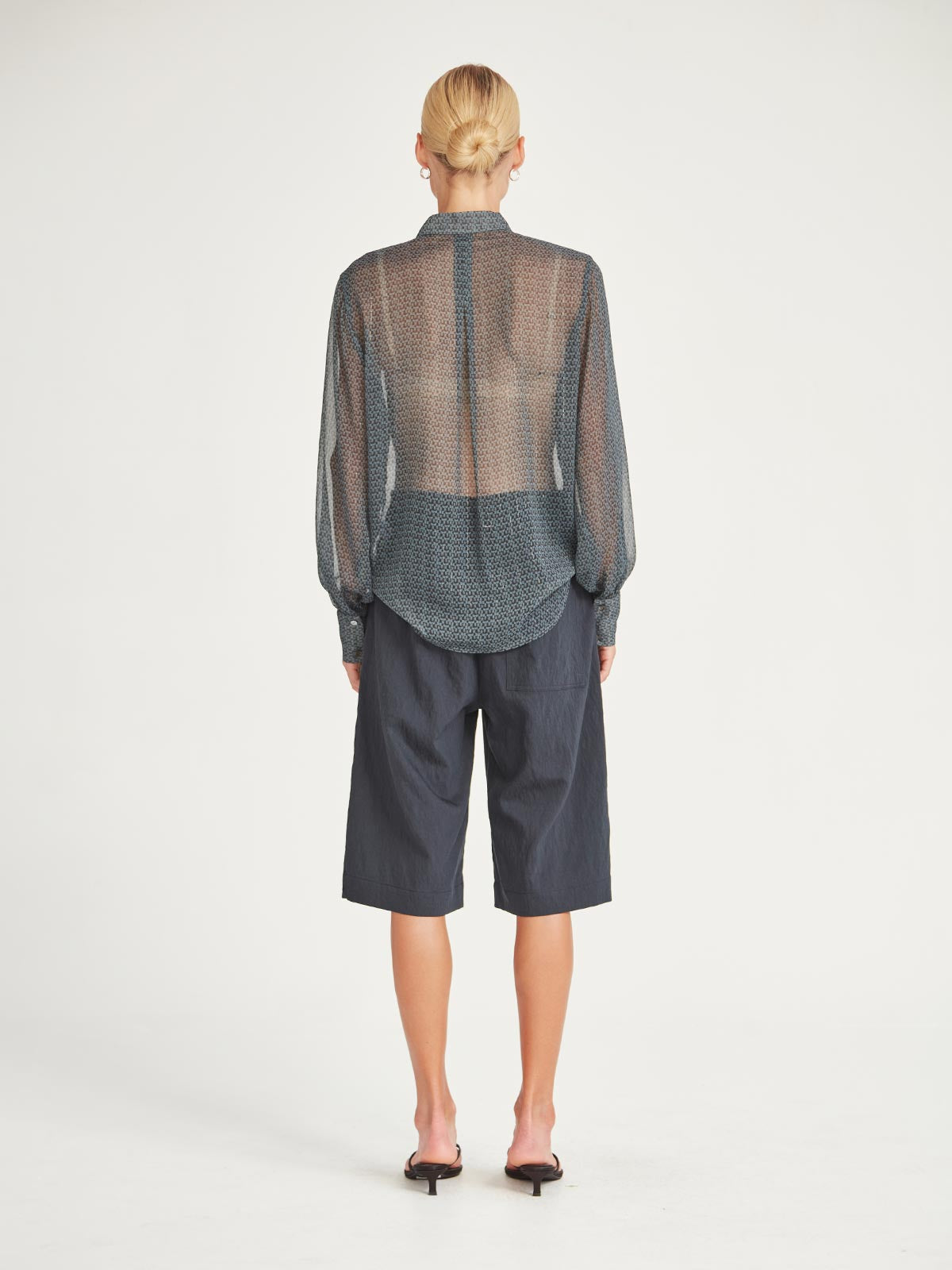Back view of the Caroline Sills Dauphine Blouse in navy print, showing sheer fabric, detailed button cuff, and flowing silhouette. Paired with navy shorts.