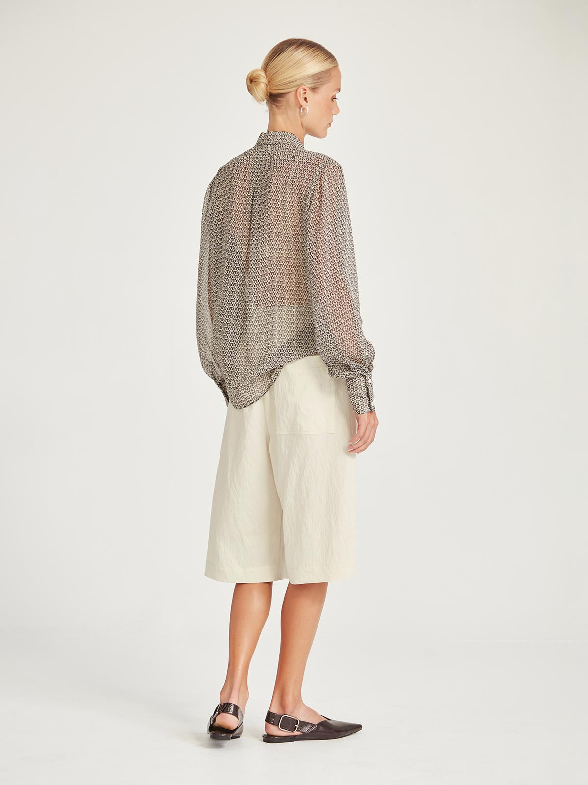 Back view of the Caroline Sills Dauphine Blouse in sand print, showing sheer fabric, detailed button cuff, and flowing silhouette. Paired with tonal chalk coloured shorts.