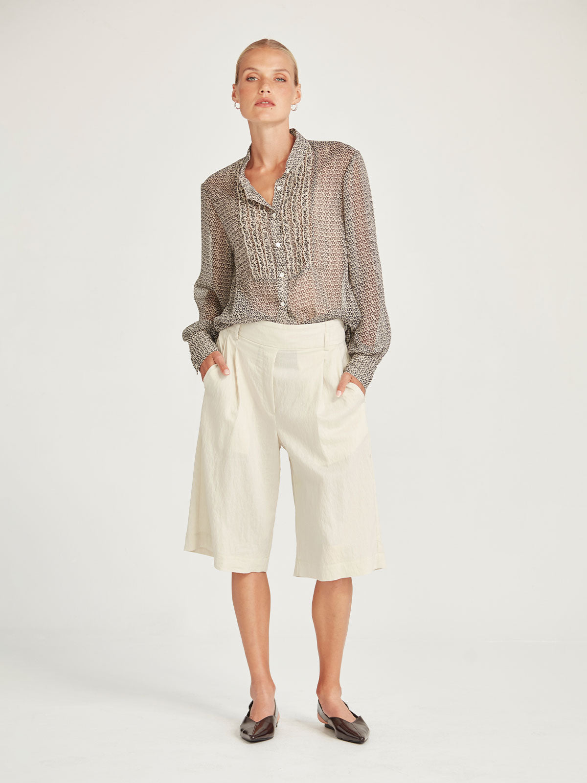 Front view of the Caroline Sills Dauphine Blouse in sand print, featuring a Mandarin collar neckline, ruffle trim detail on the bust and sheer long sleeves. Styled with chalk coloured tonal shorts.