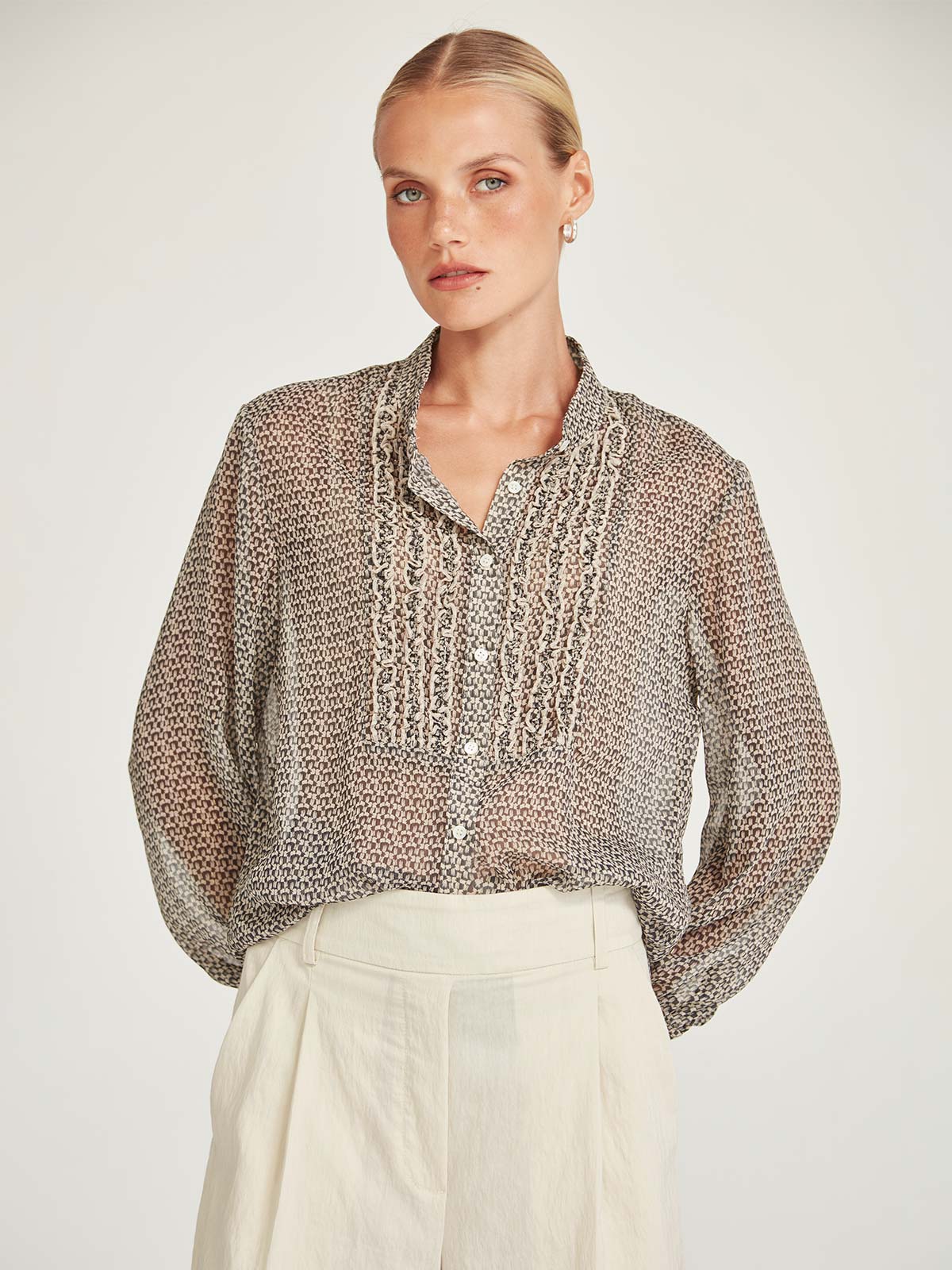 Close-up front view of the Caroline Sills Dauphine Blouse in sand print, featuring a Mandarin collar neckline, ruffle trim detail on the bust, and sheer long sleeves. 