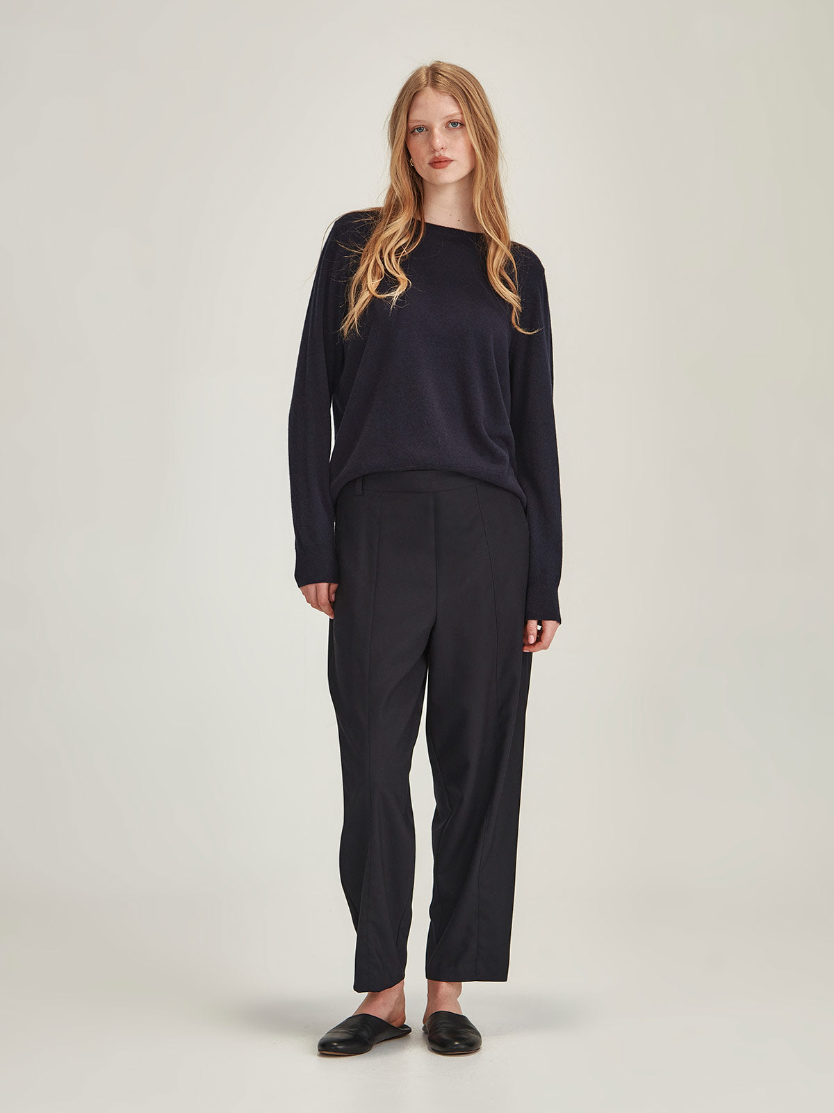 Blonde woman wearing the Caroline Sills  Tobi Pant in navy paired with the Caroline  Eleanor Cashmere Sweater in french navy on a grey background.
