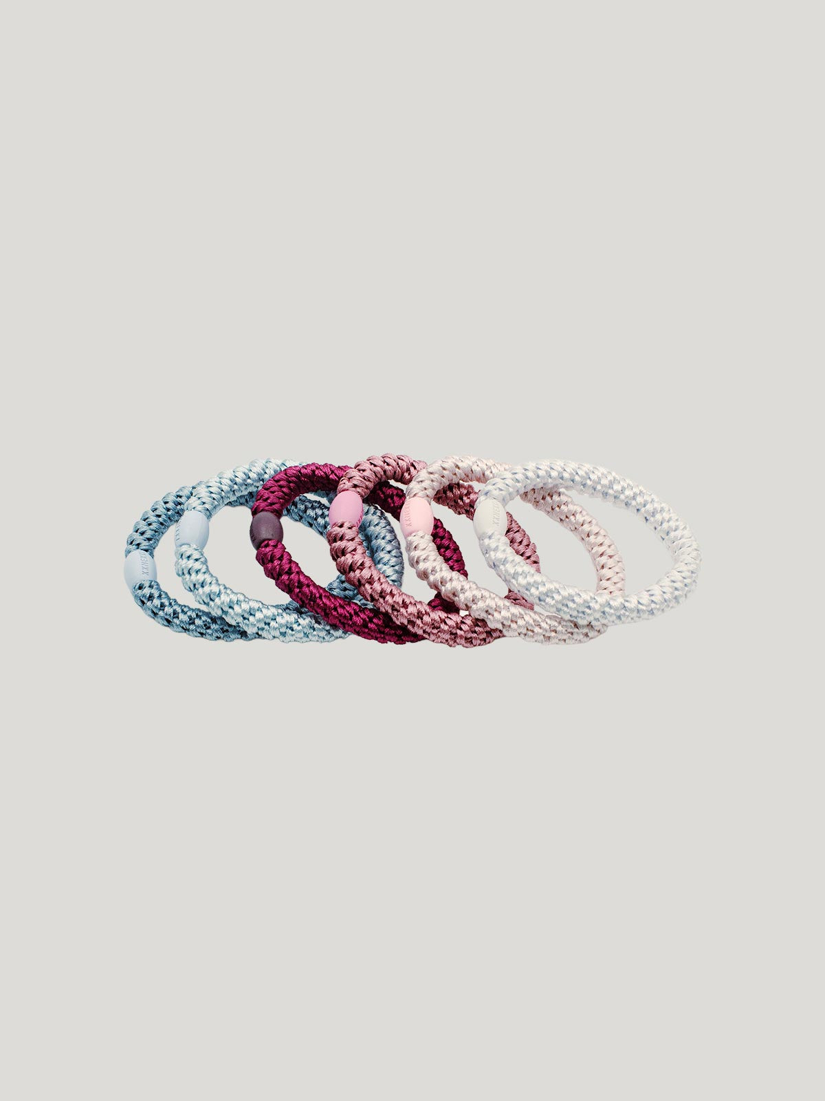 Set of six braided hair ties in different pink and blues colours on a light gray background