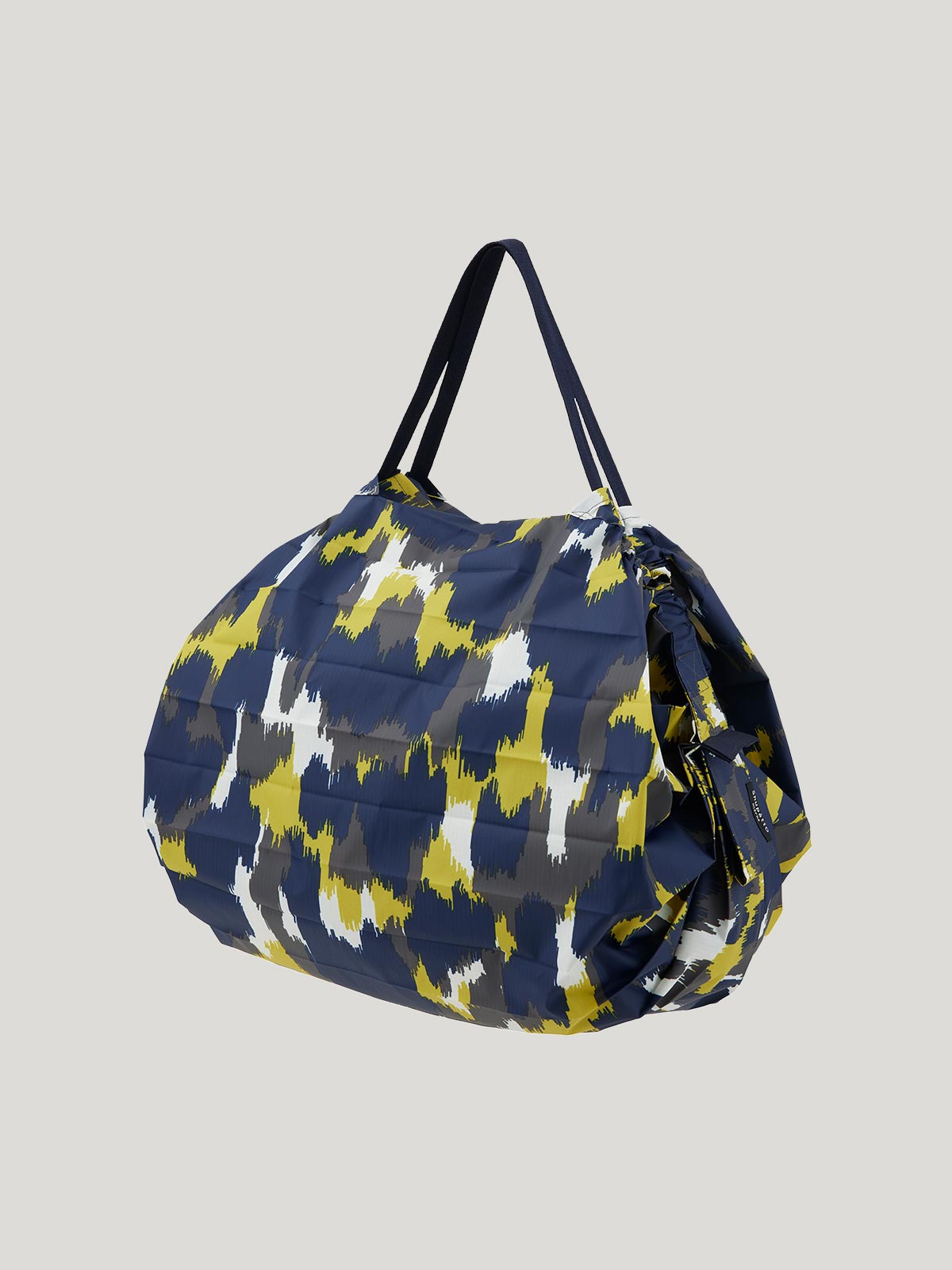 Foldable, reusable shopping bag with a blue, yellow, grey and white patterned design on a grey background.