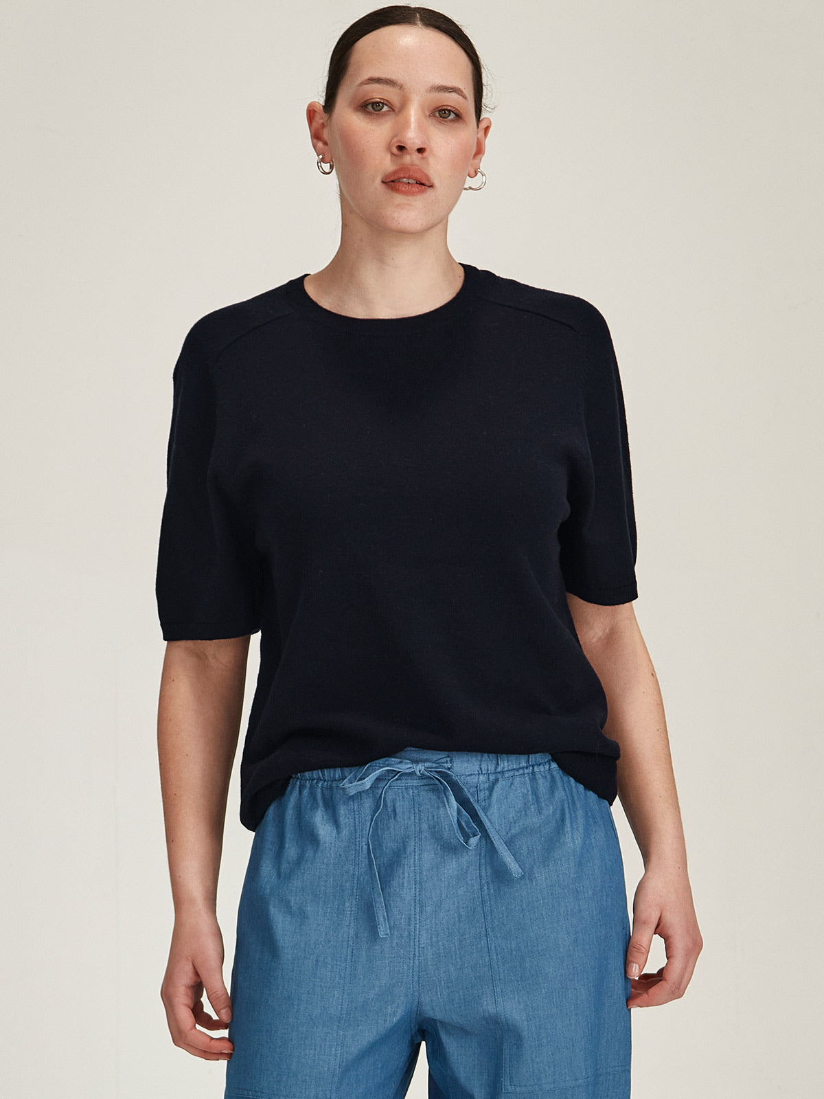 close up of a woman wearing a navy Sills Cecilia knitted Tee t-shirt on grey background
