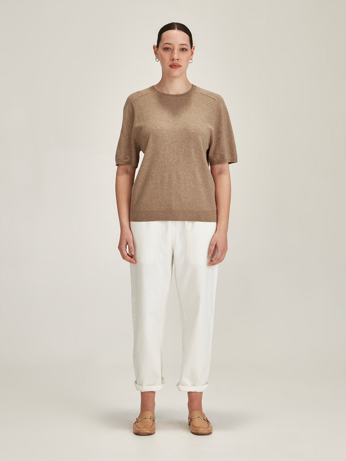 woman wearing a beige Sills Cecilia knitted Tee t-shirt and white denim Ginza cropped jeans on grey background