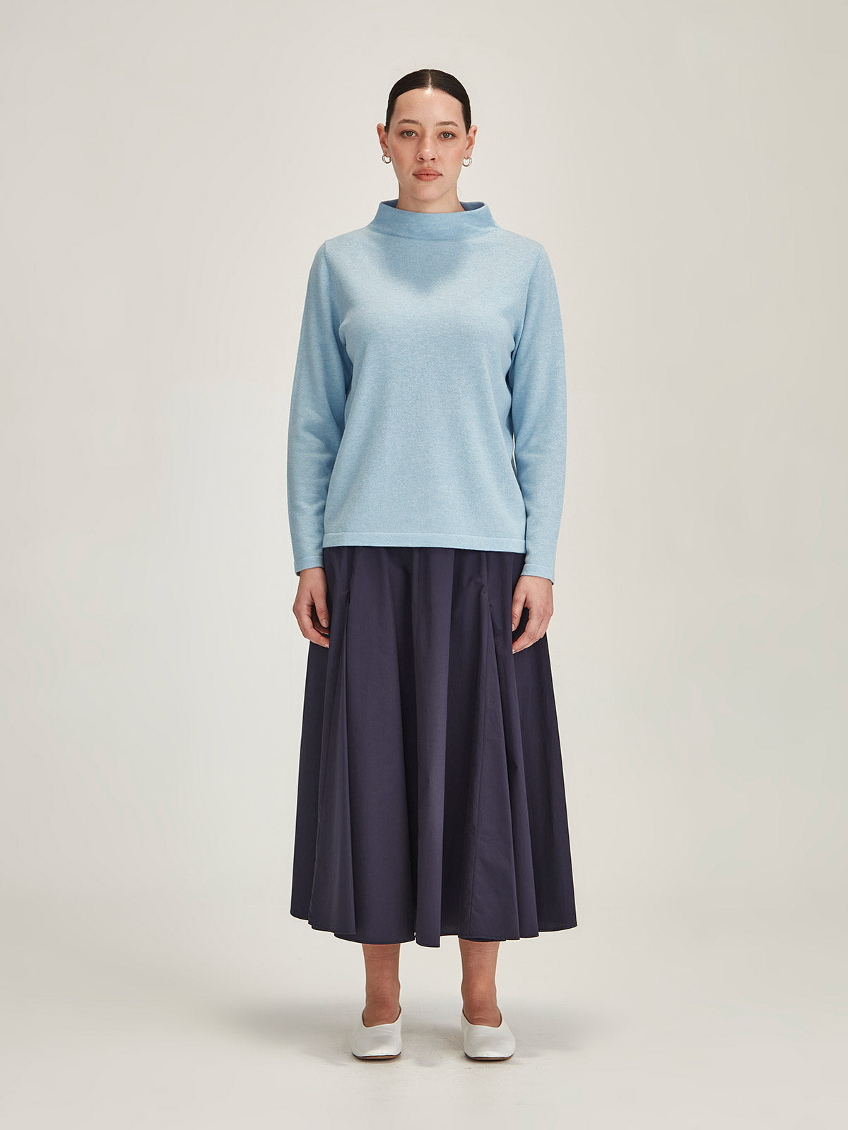woman wearing sky blue Sills Tasmin funnel neck sweater with navy Zaiya godet midi skirt against grey background